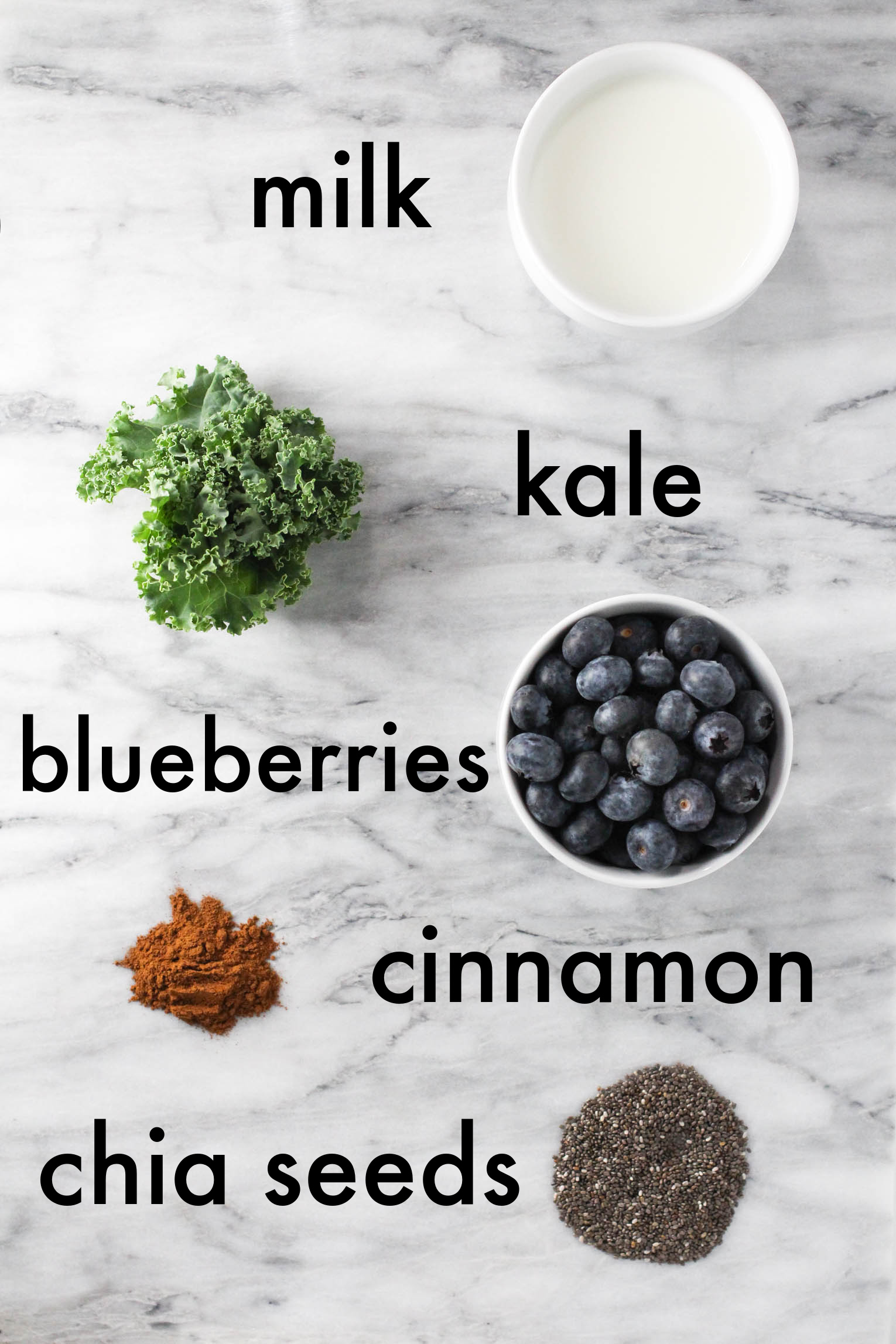 Overhead shot of the smoothy ingredients. The ingredients are labled with text overlay as follows: milk, kale, blueberries, cinnamon, chia seeds.