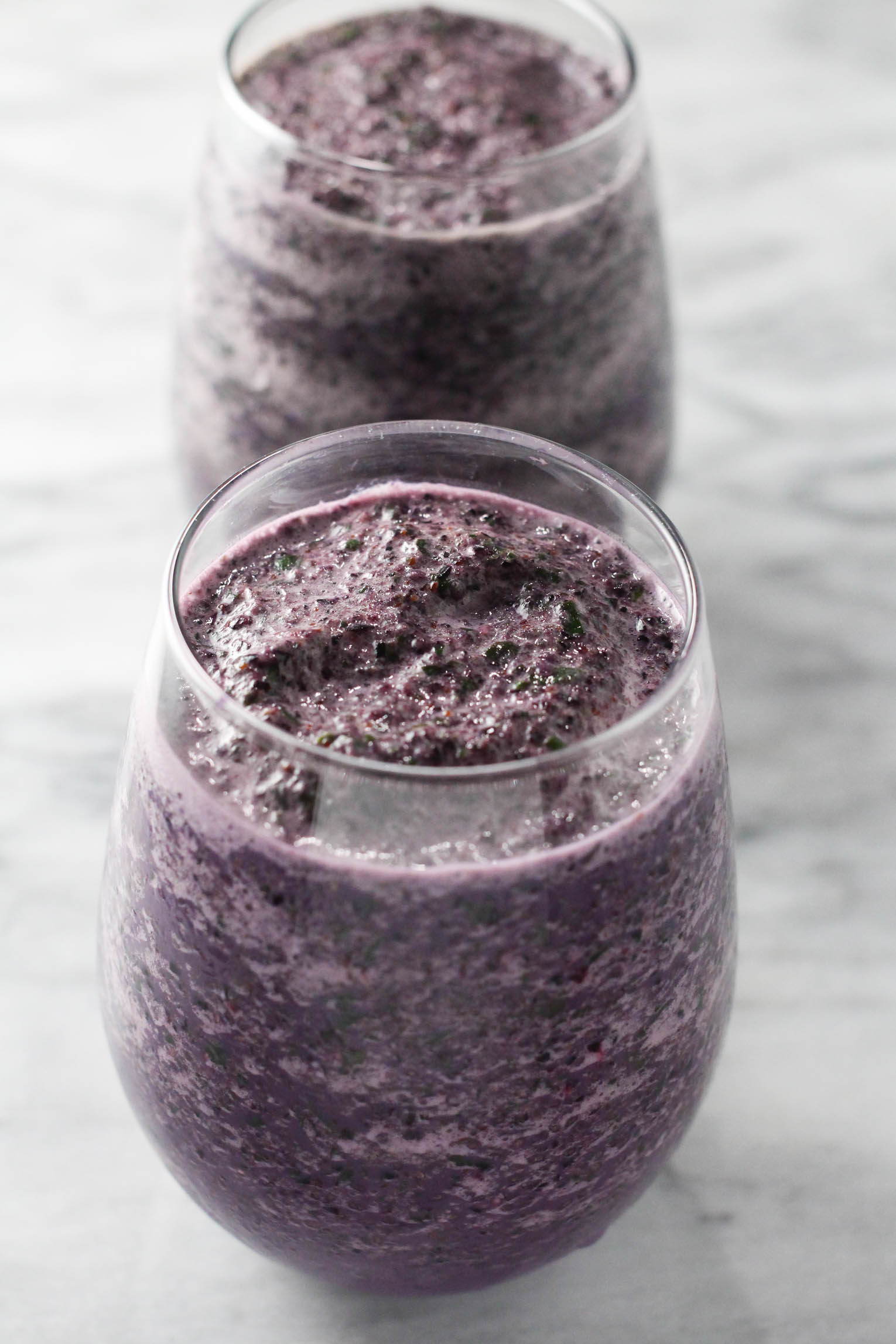 Close up shot of the blueberry kale smoothie in a glass. There is another glass with the smoothie in the background.