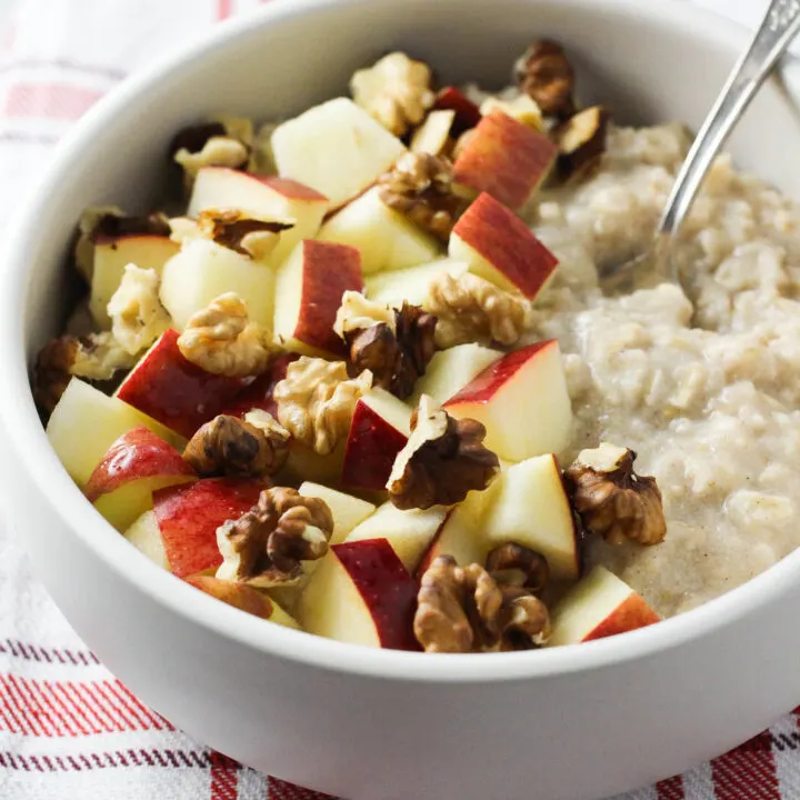 Applesauce oatmeal in a bowl, garnished with apples and wallnuts.