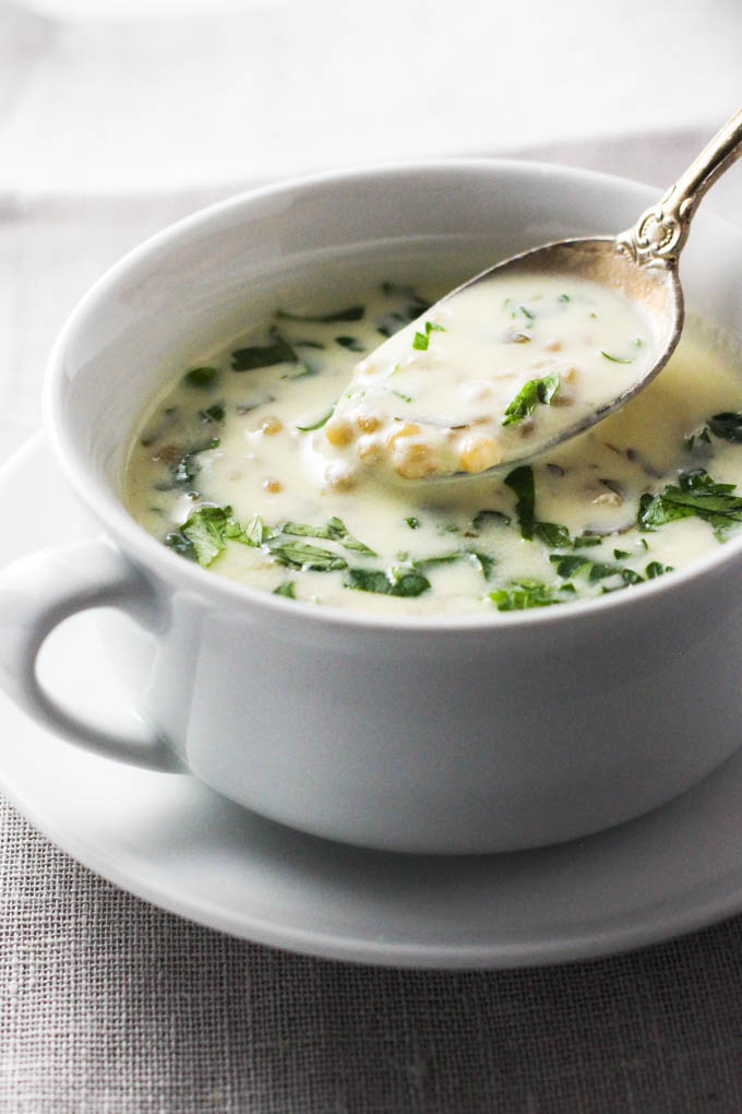 A white bowl with a creamy soup and a silver spoon with soup.