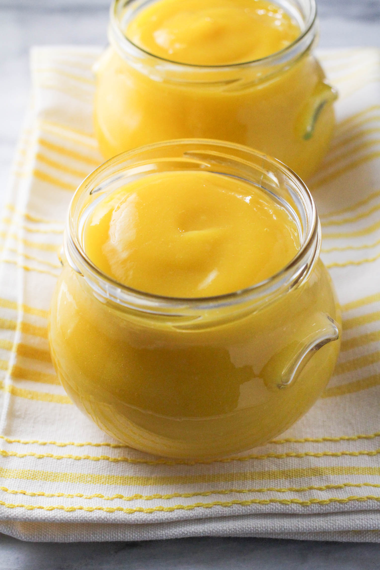 Two jars with mango puree standing on a kichen towel.