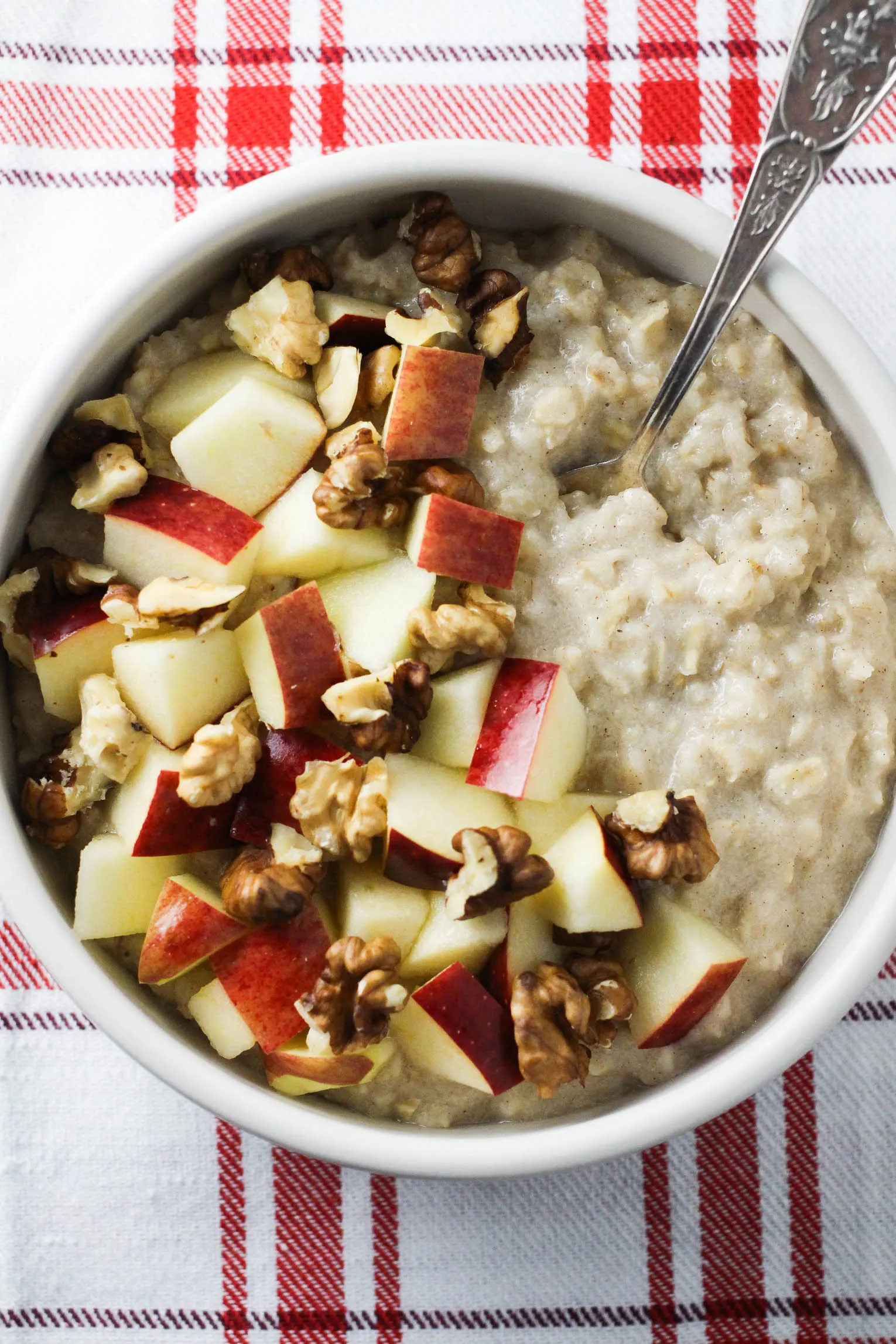 Overhead shot of oatmeal in a bowl garnished with apples and walnuts. There is a silver spoon in the oats.