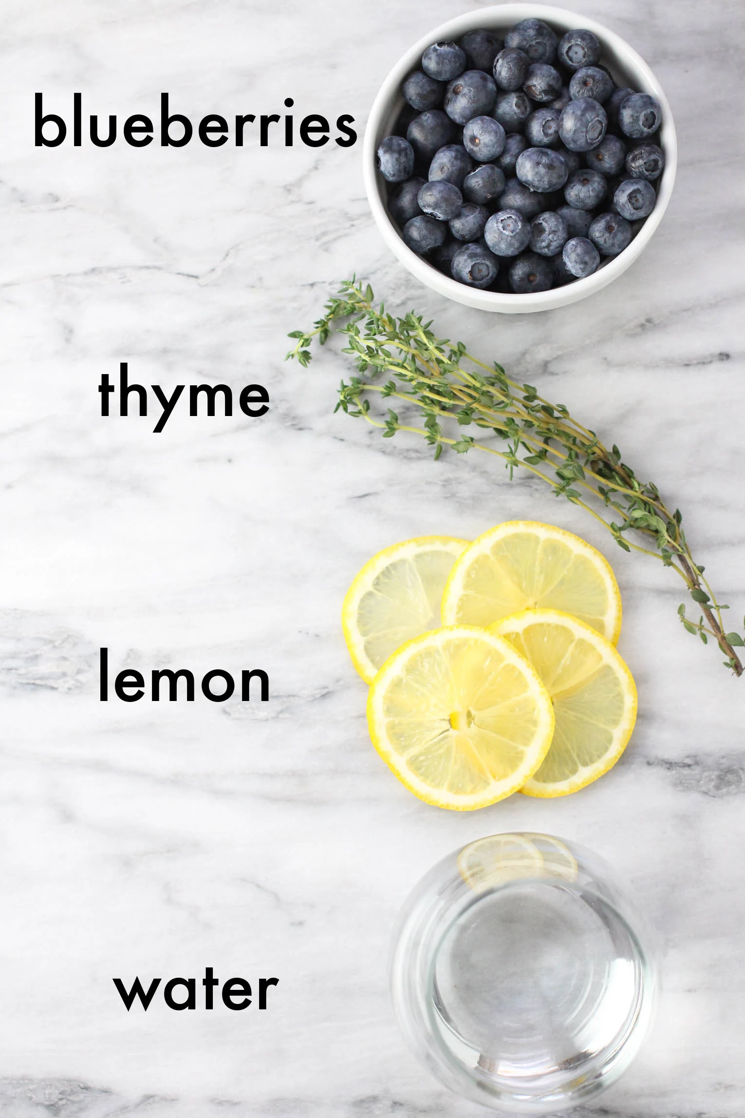 Ingredients for the blueberry water on marble background. The text overlay as follows: blueberries, thyme, lemon, water.