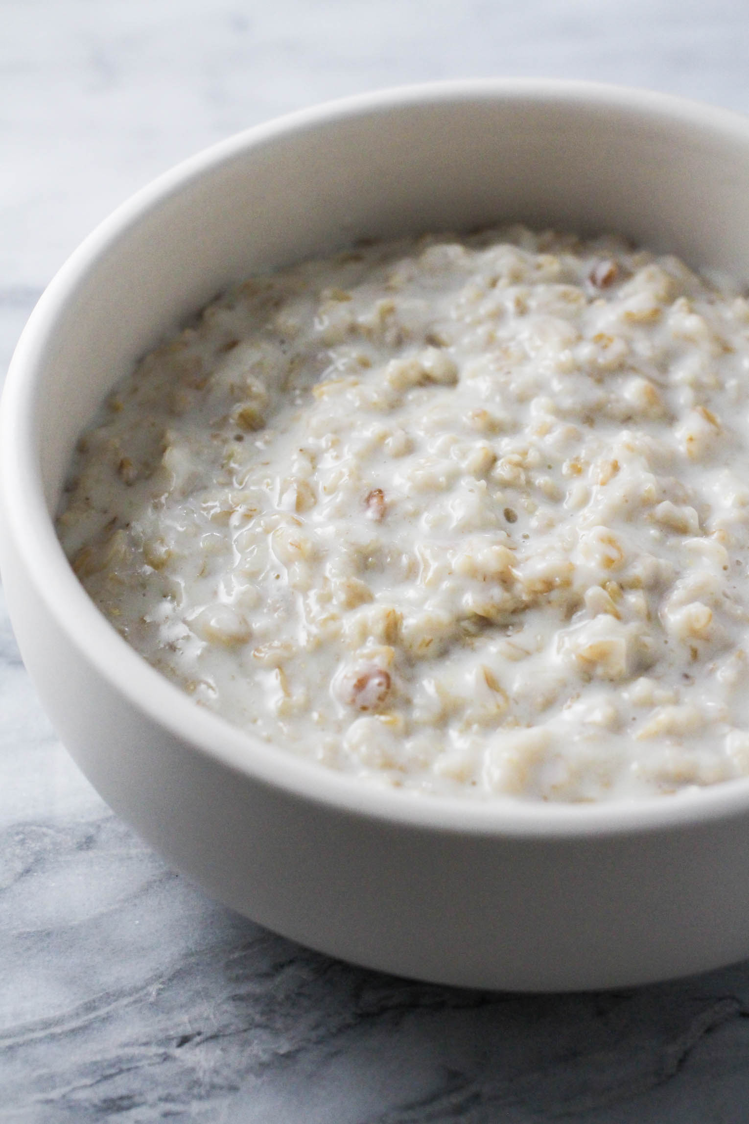 Creamy oatmeal in a bowl standing on marble background.