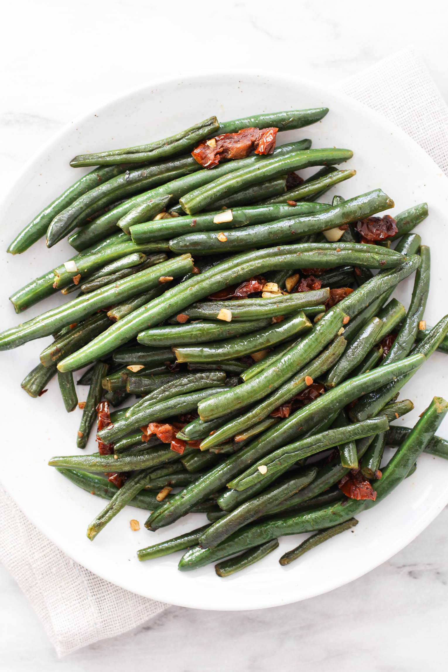 Green beans with sun-dried tomatoes and garlic on a white plate.