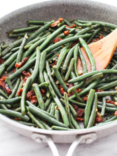 Green beans with sun-dried tomatoes and garlic in a skillet.