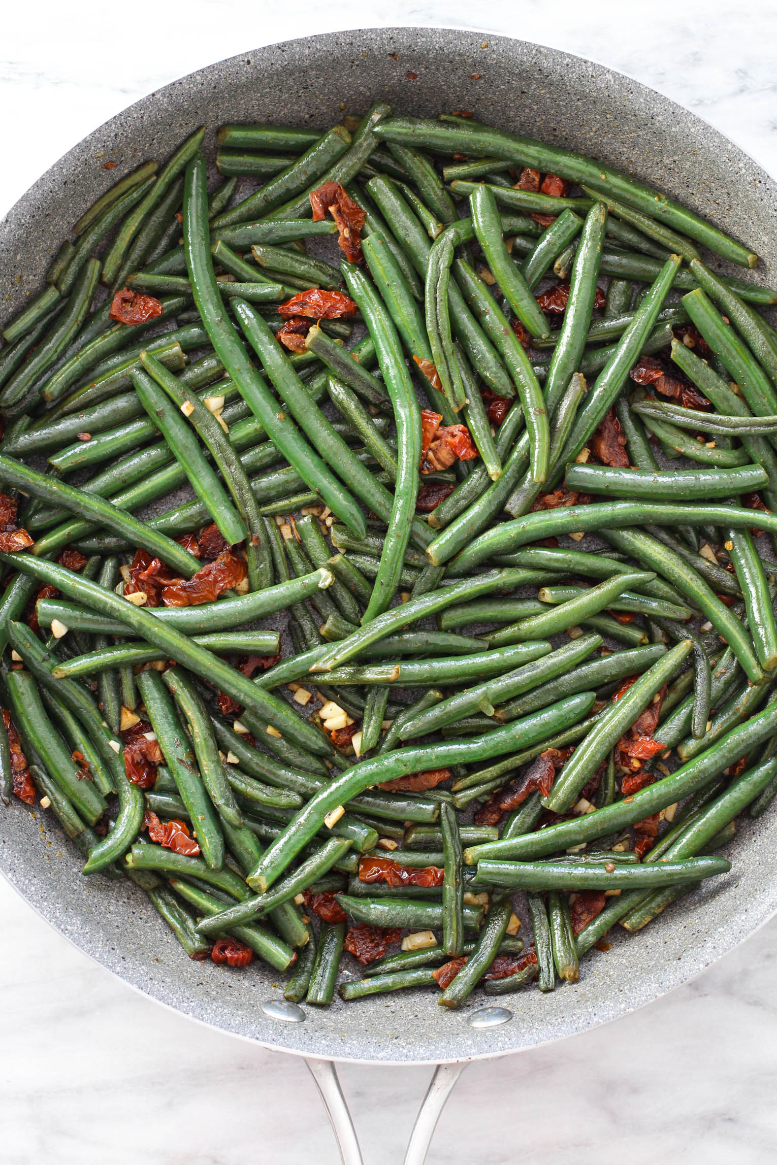 Overhead shot of green beans with sun-dried tomatoes and garlic in a skillet.