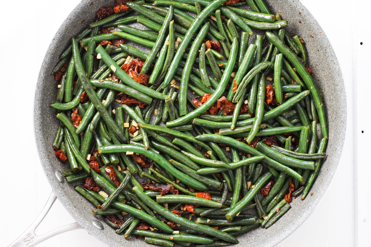 Overhead shot of green beans with sun-dried tomatoes and garlic in a skillet.