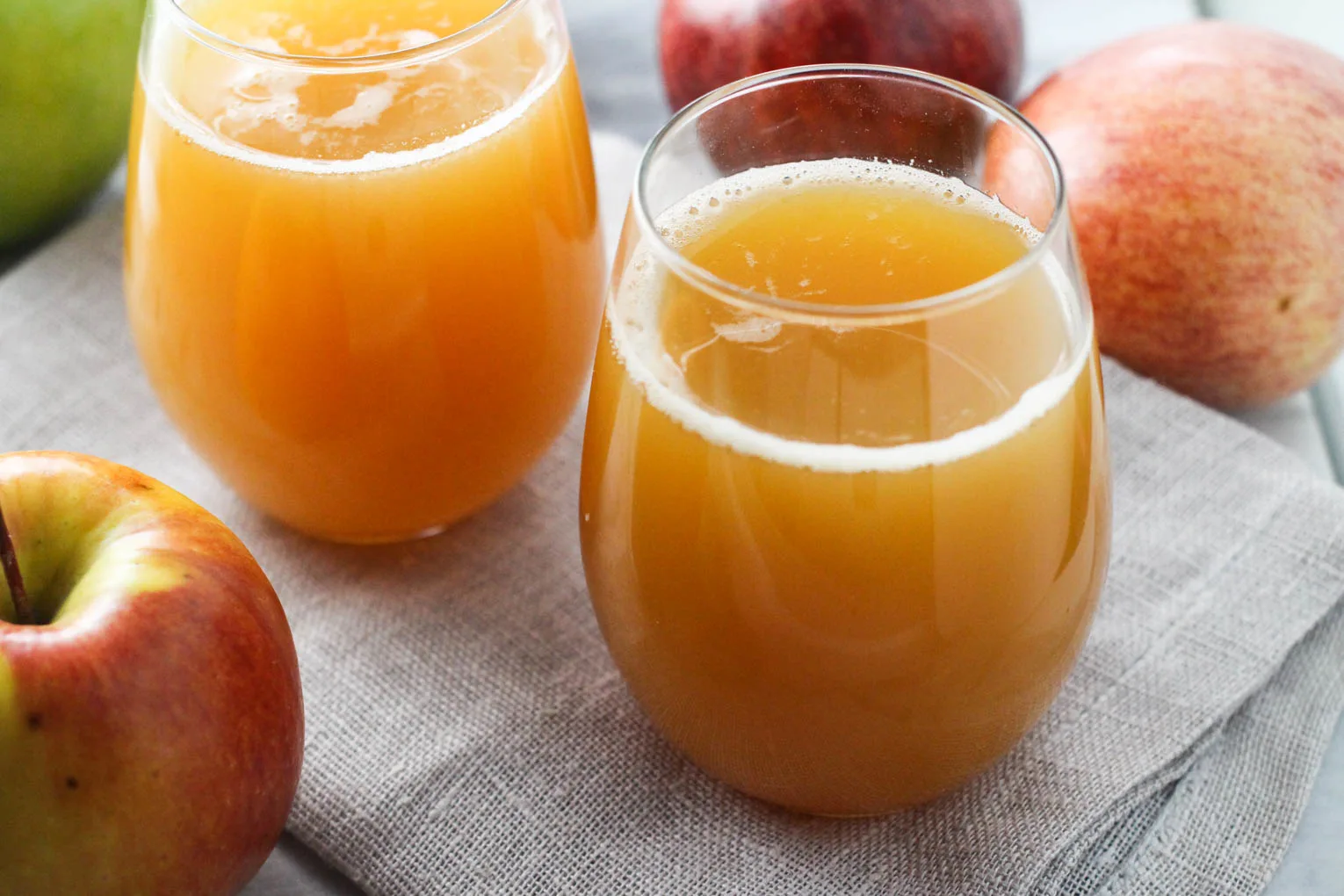 Two glasses with apple juice standing on a linen napkin. Apples are placed around the glasses.