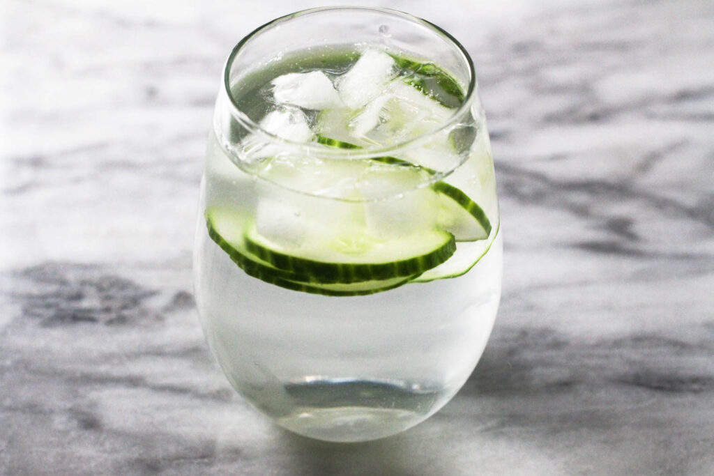 A glass with water, cucumber slices and ice on marble background.