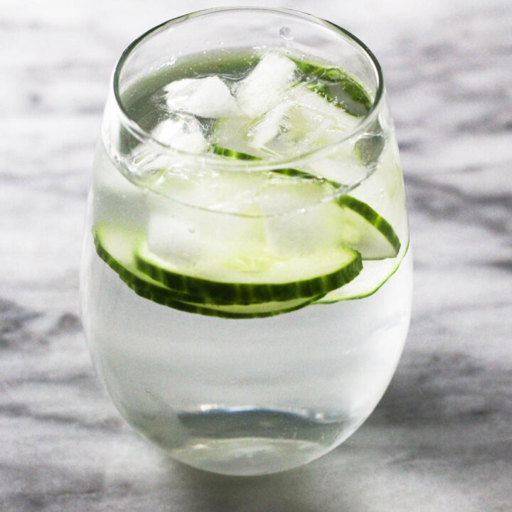 A glass with water, cucumber slices and ice on marble background.