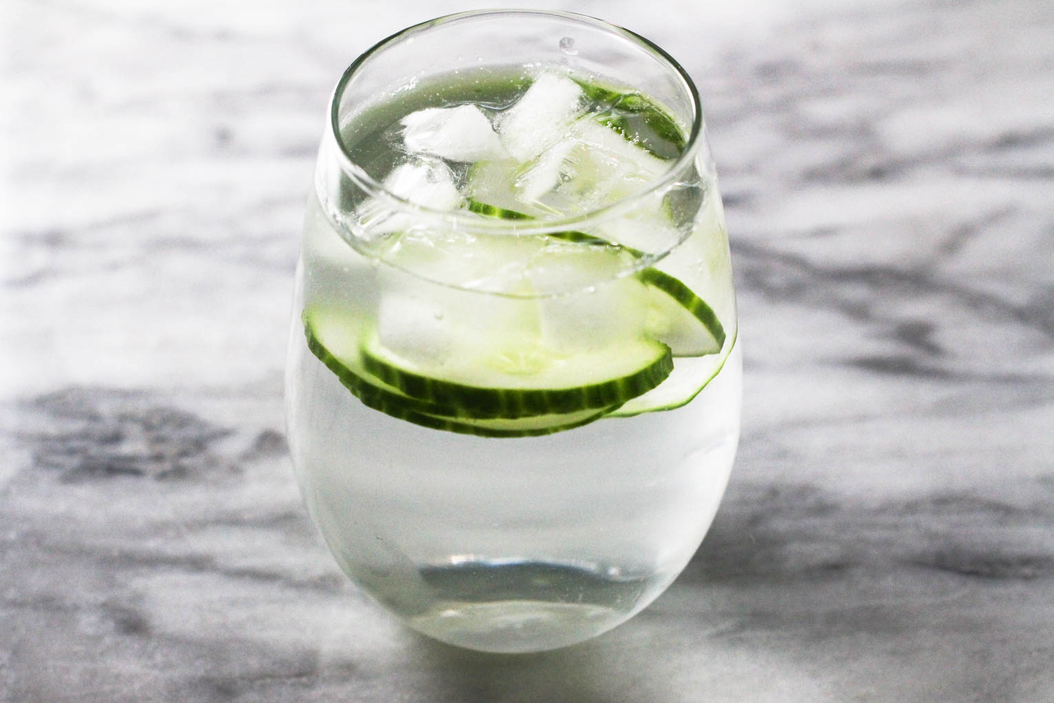 A glass with water, cucumber slices and ice on the marble background.