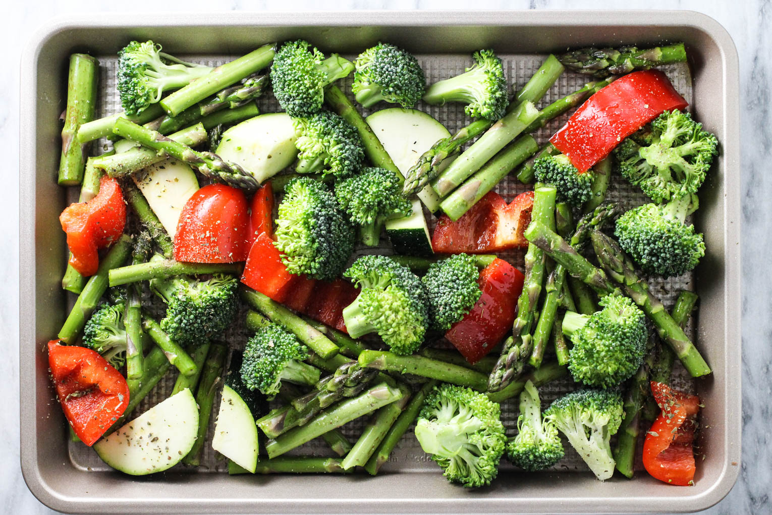 Mixed vegetables on a baking sheet, seasoned with spices and olive oil.