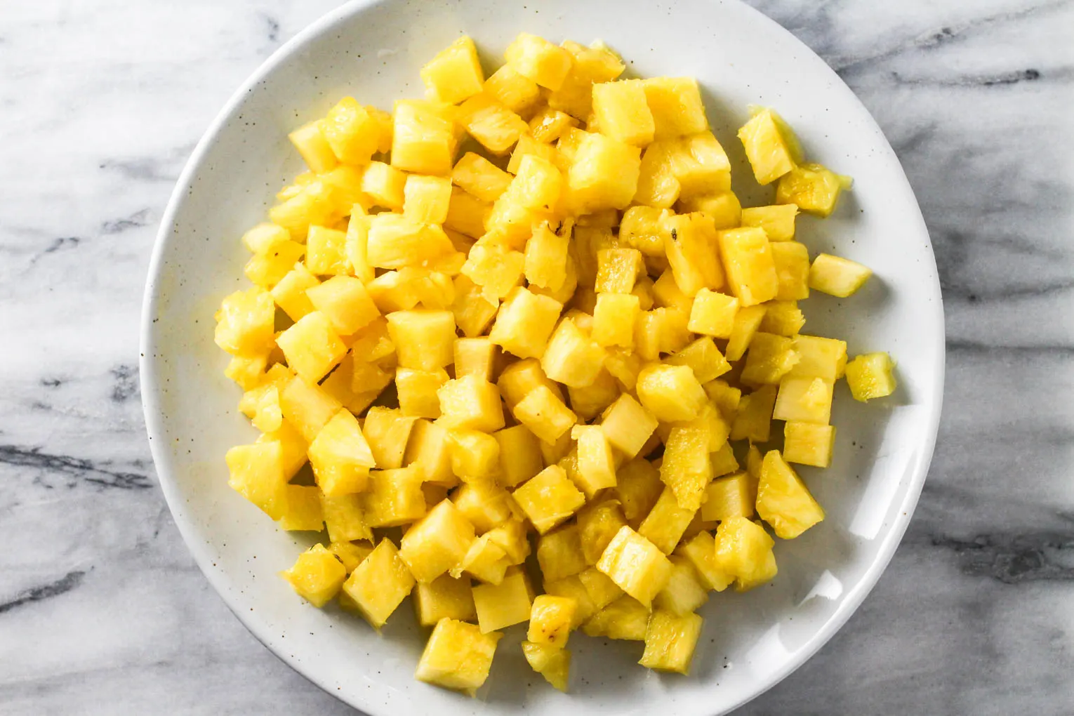 Overhead shot of diced pineapple on a plate standing on marble background.