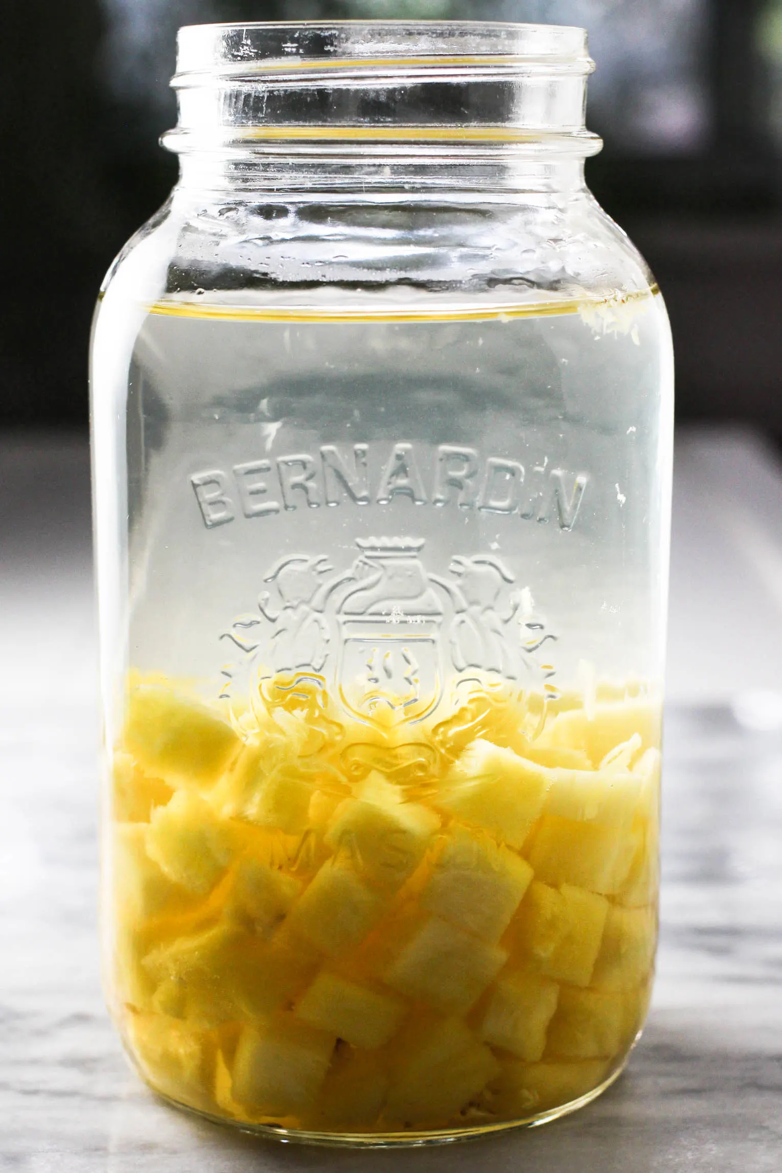 A Mason jar with pineapple water and small pieces of pineapple on the bottom.