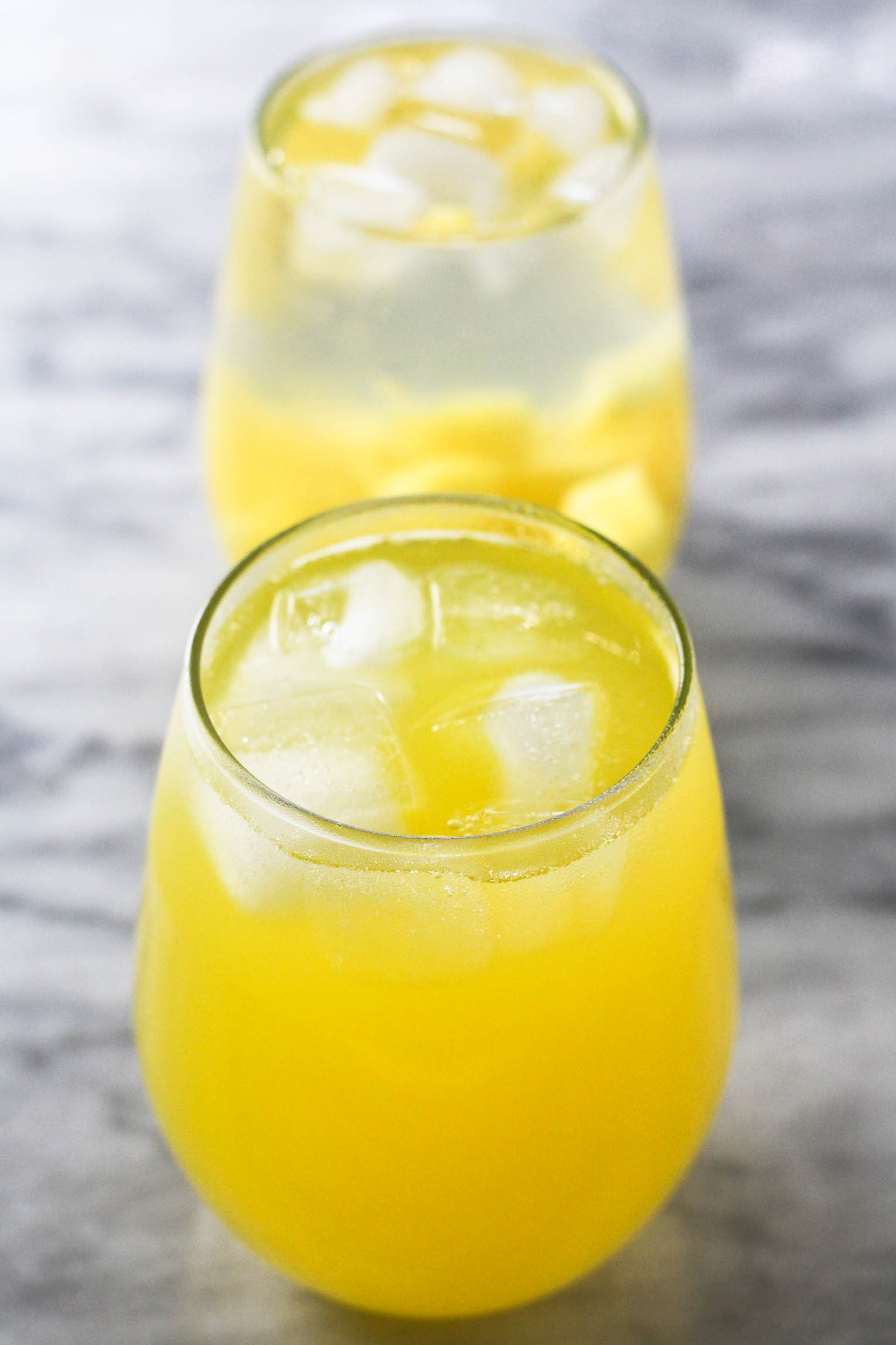 Two glasses of pineapple water with ice cubes. The glasses are standing on marble background.
