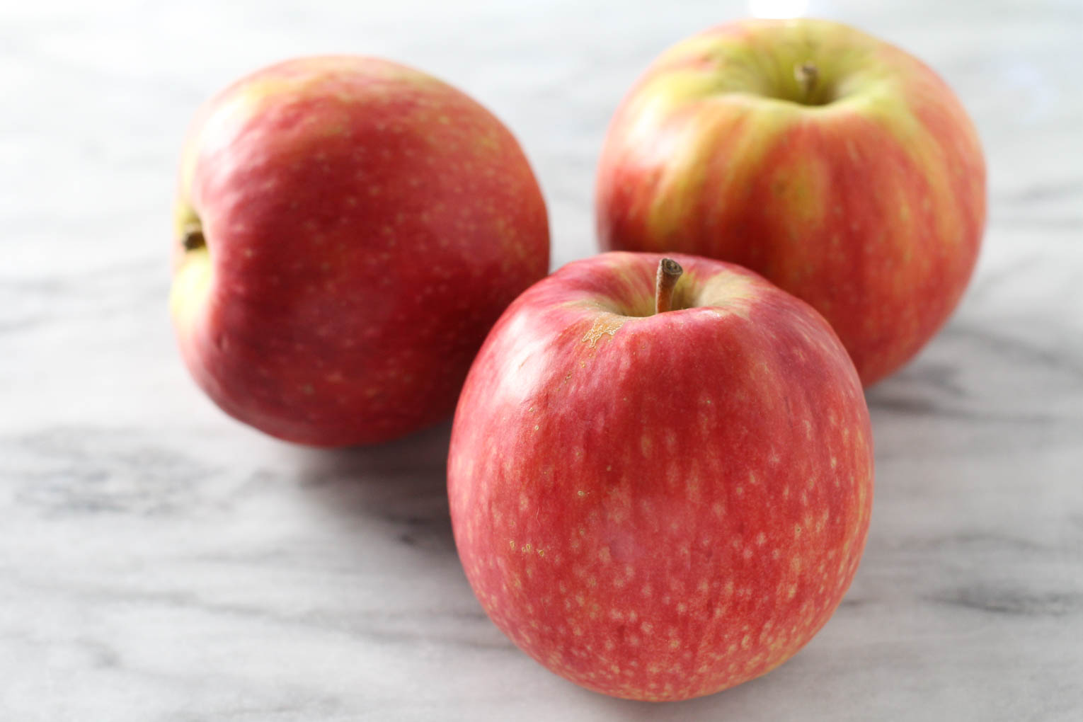 Three Pink Lady apples on marble background.