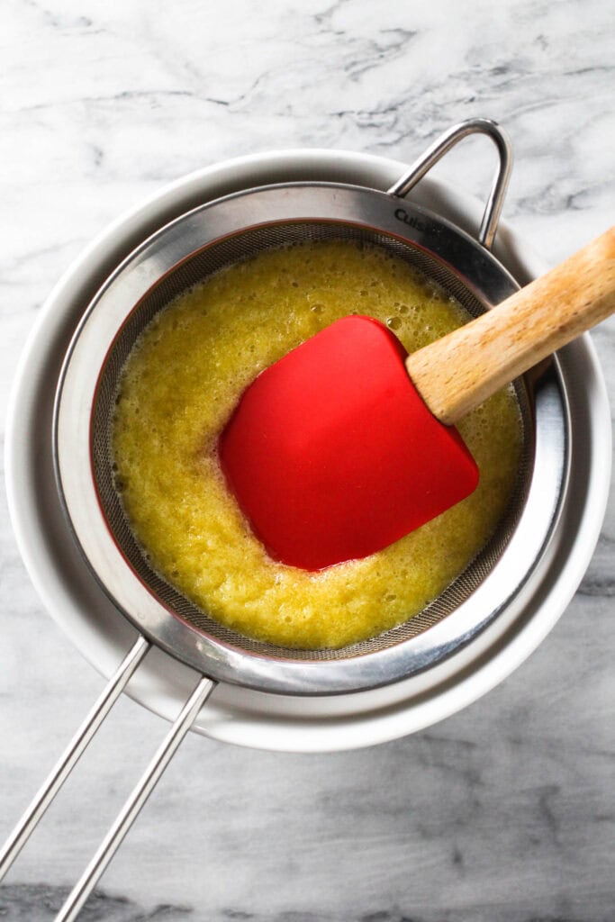 Straining blended pineapple through mesh strainer.