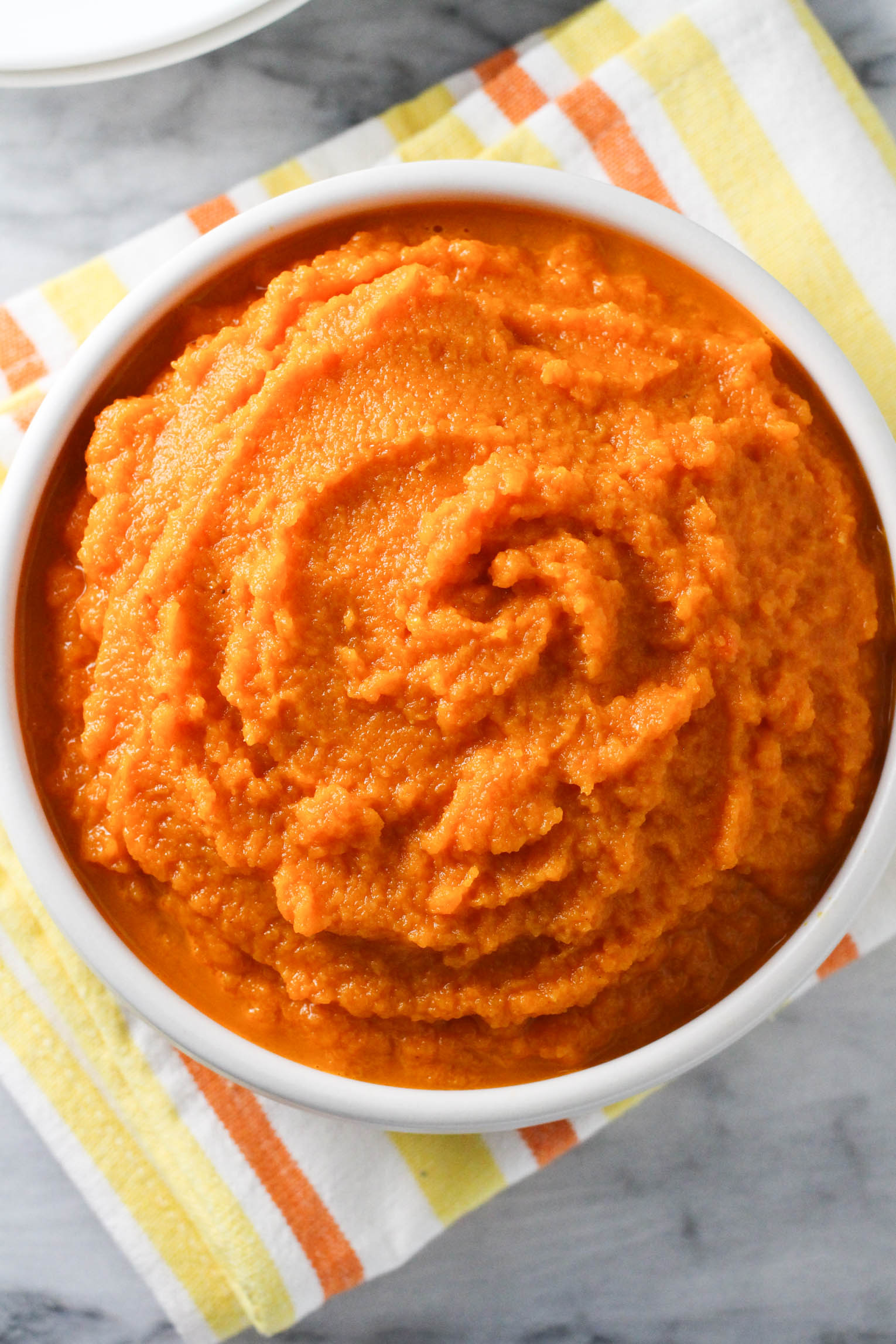 Overhead shot of mashed carrots in a bowl standing on a tea towel.