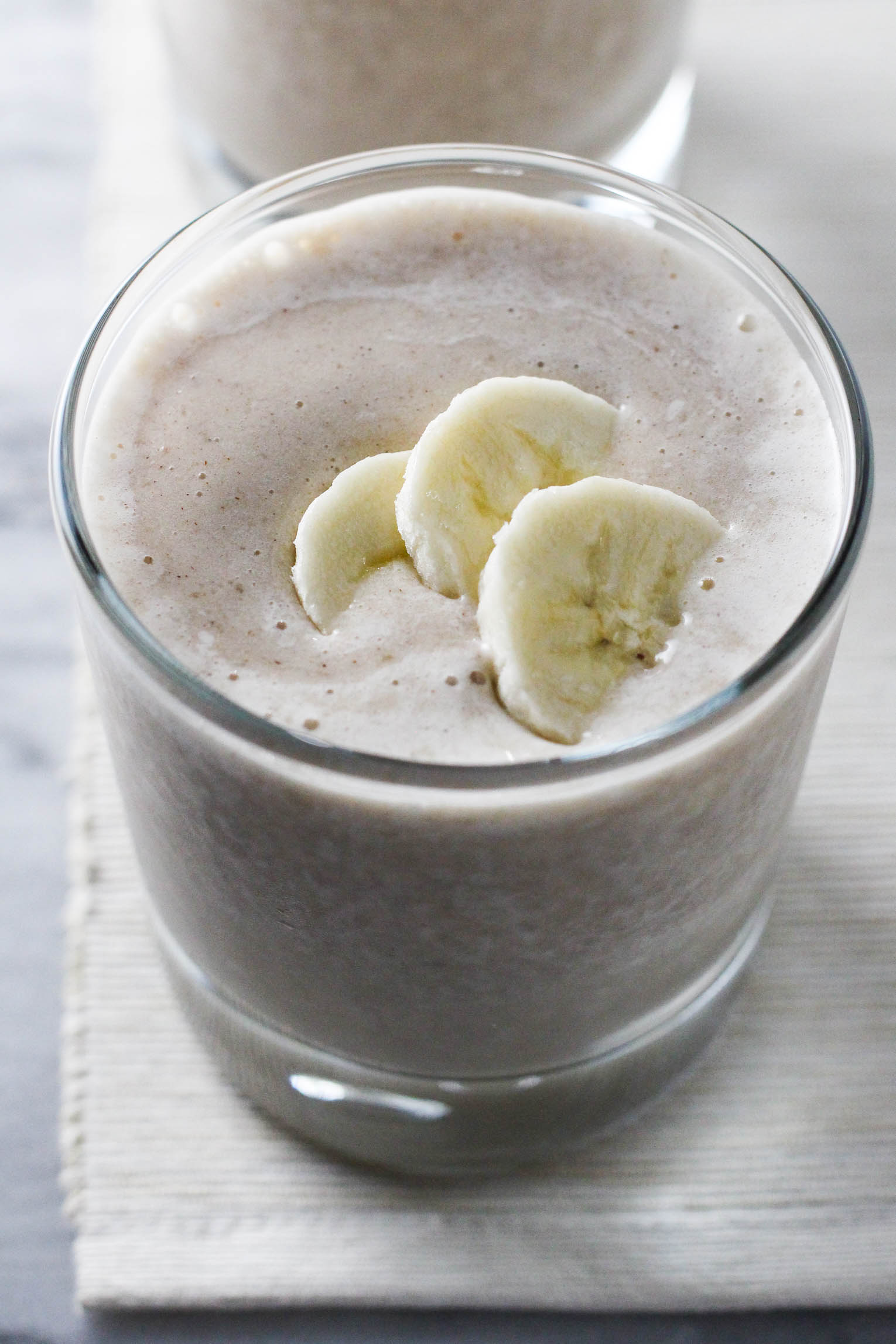 Close up shot of a glass of banana smoothie granished with three banana slices.