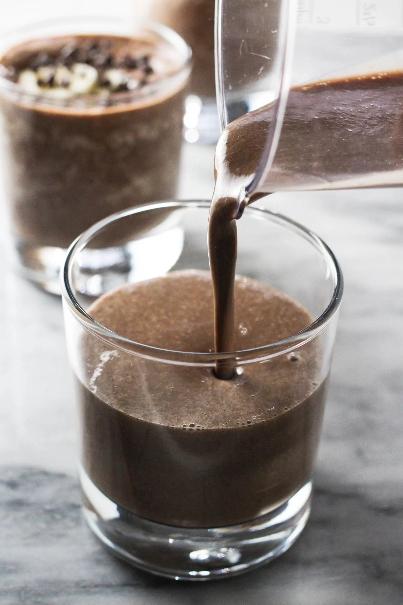 Chocolate banana smoothie being poured into a glass. Another glass in the background.