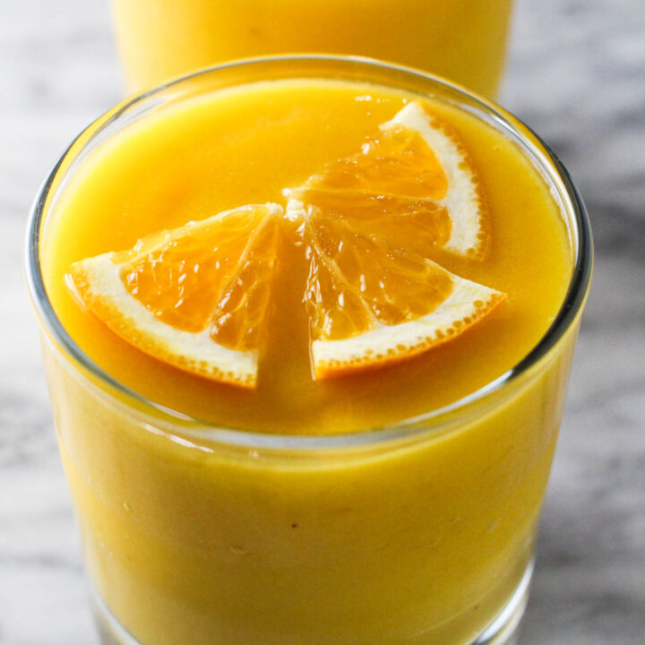 A glass of orange mango smoothie garnished with orange slices.