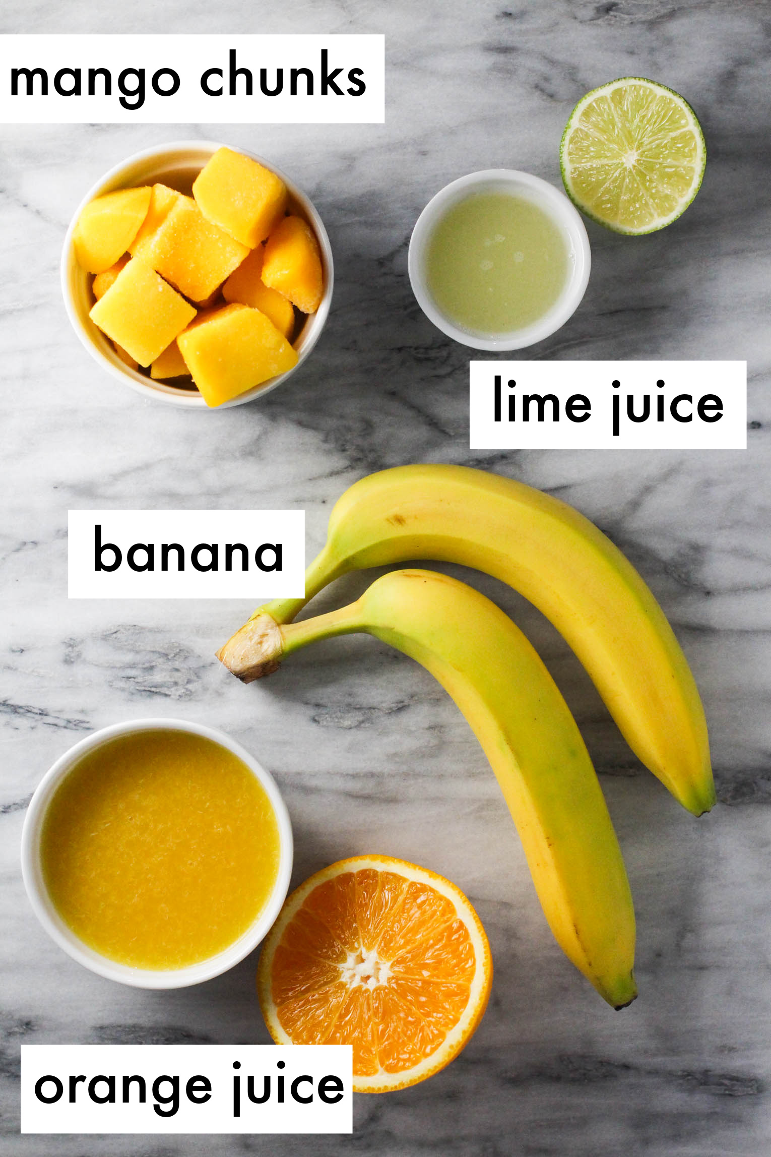 Ingredients for orange mango smoothie on marble background. The ingredients are labeled as follows: mango chuncks, lime juice, banana, orange juice.