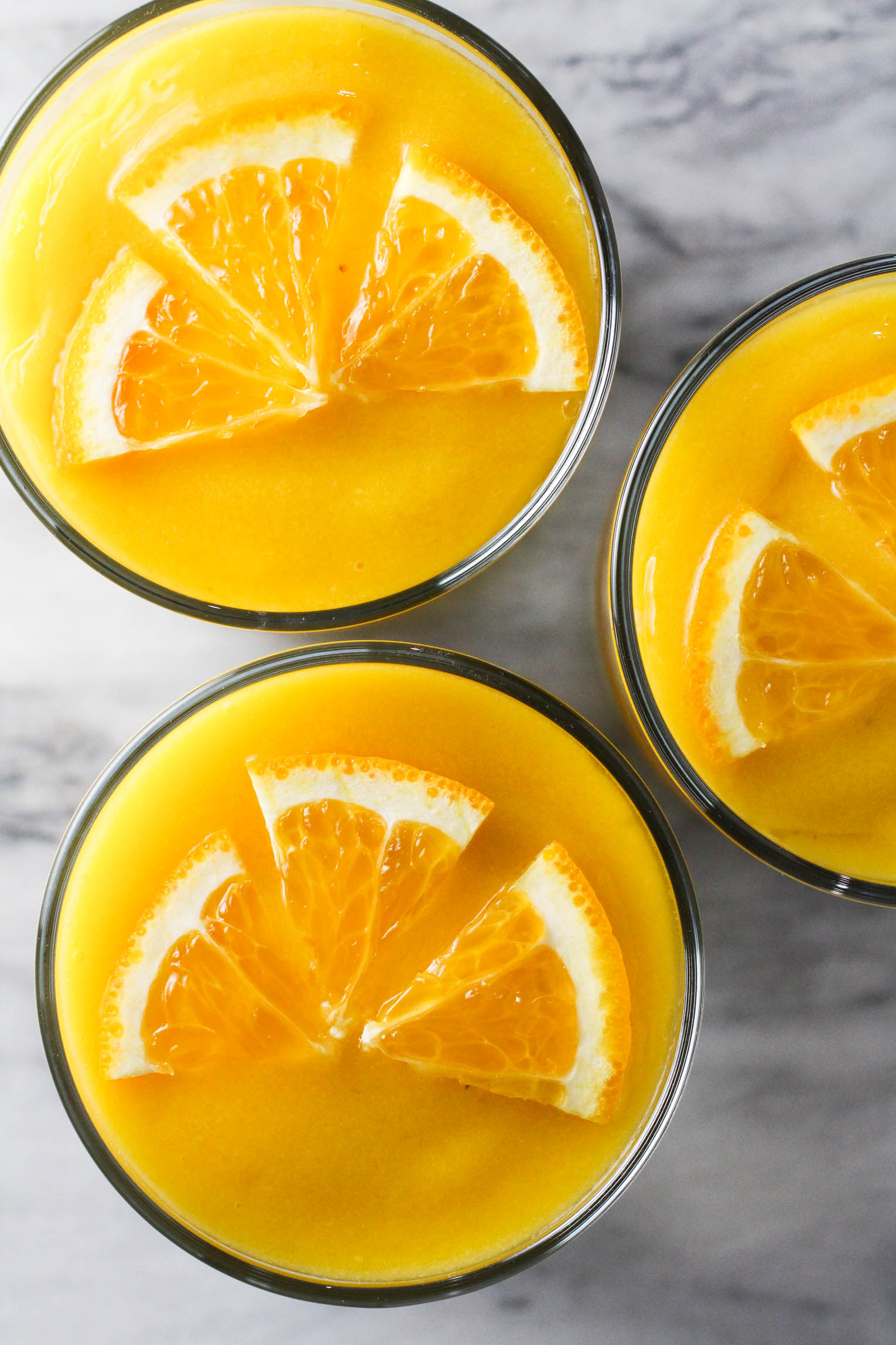 Overhead shot of three glasses of orange mango smoothie garnished with orange slices.