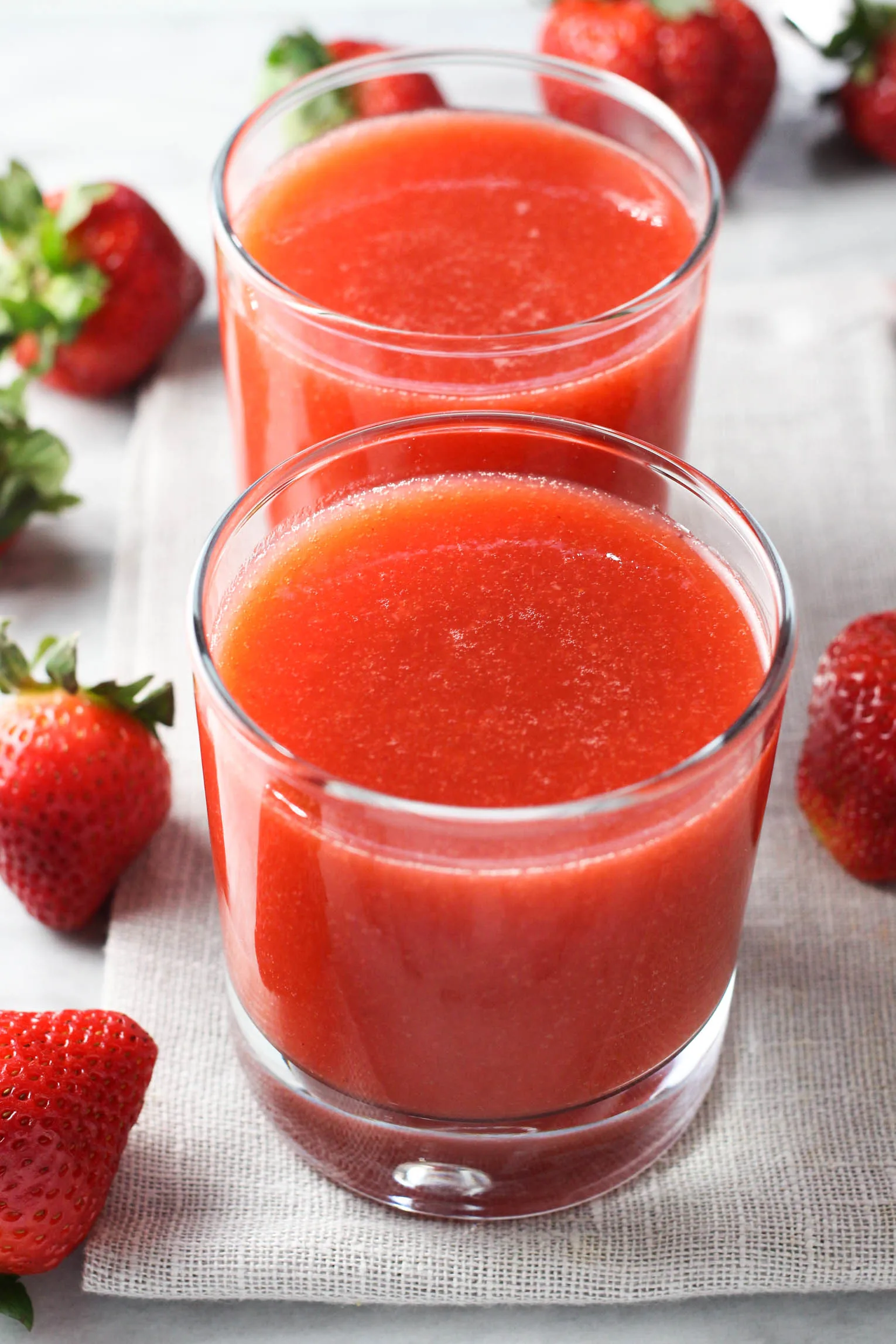 Two glasses of strawberry juice. A few fresh strawberries around them.