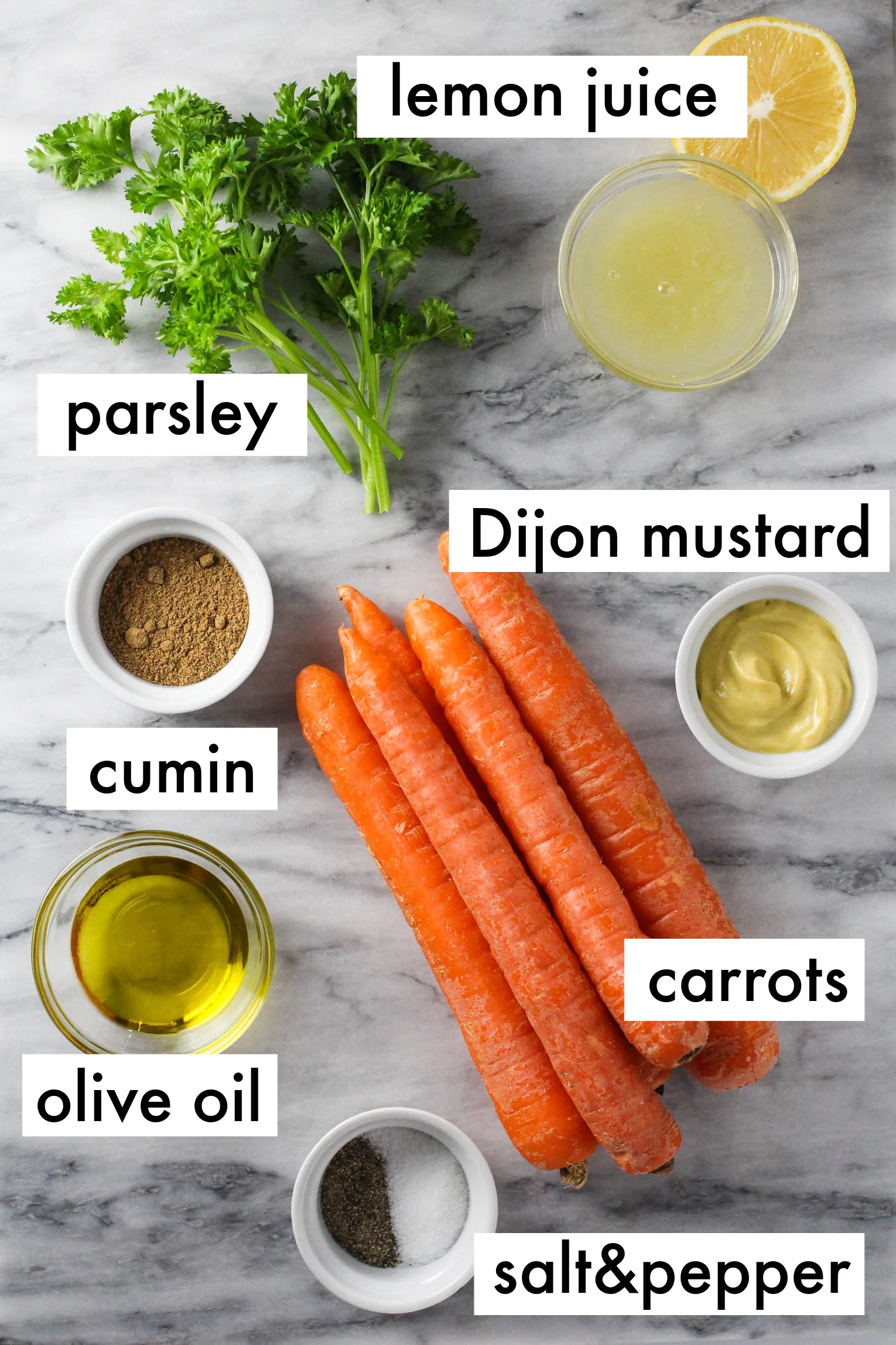 Ingredients for the French carrot salad displayed on a marble background. The ingredients are listed as follows: lemon juice, parsley, Dijon mustard, cumin, carrots, olive oil, salt and pepper.
