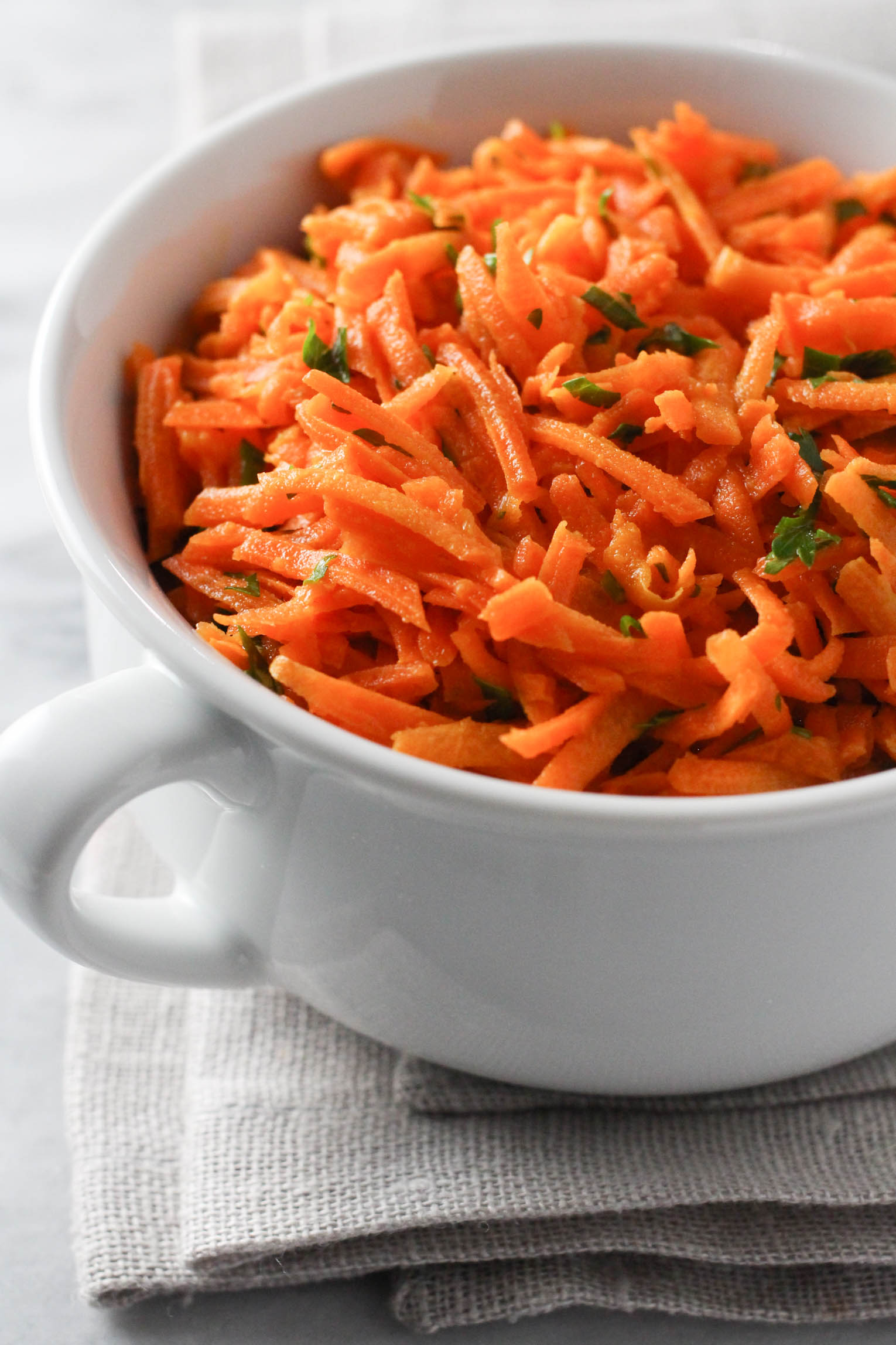 French grated carrot salad in a white bowl standing on a linen napkin.