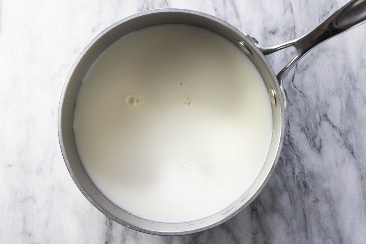 Overhead shot of a saucepan with milk standing on marble background.