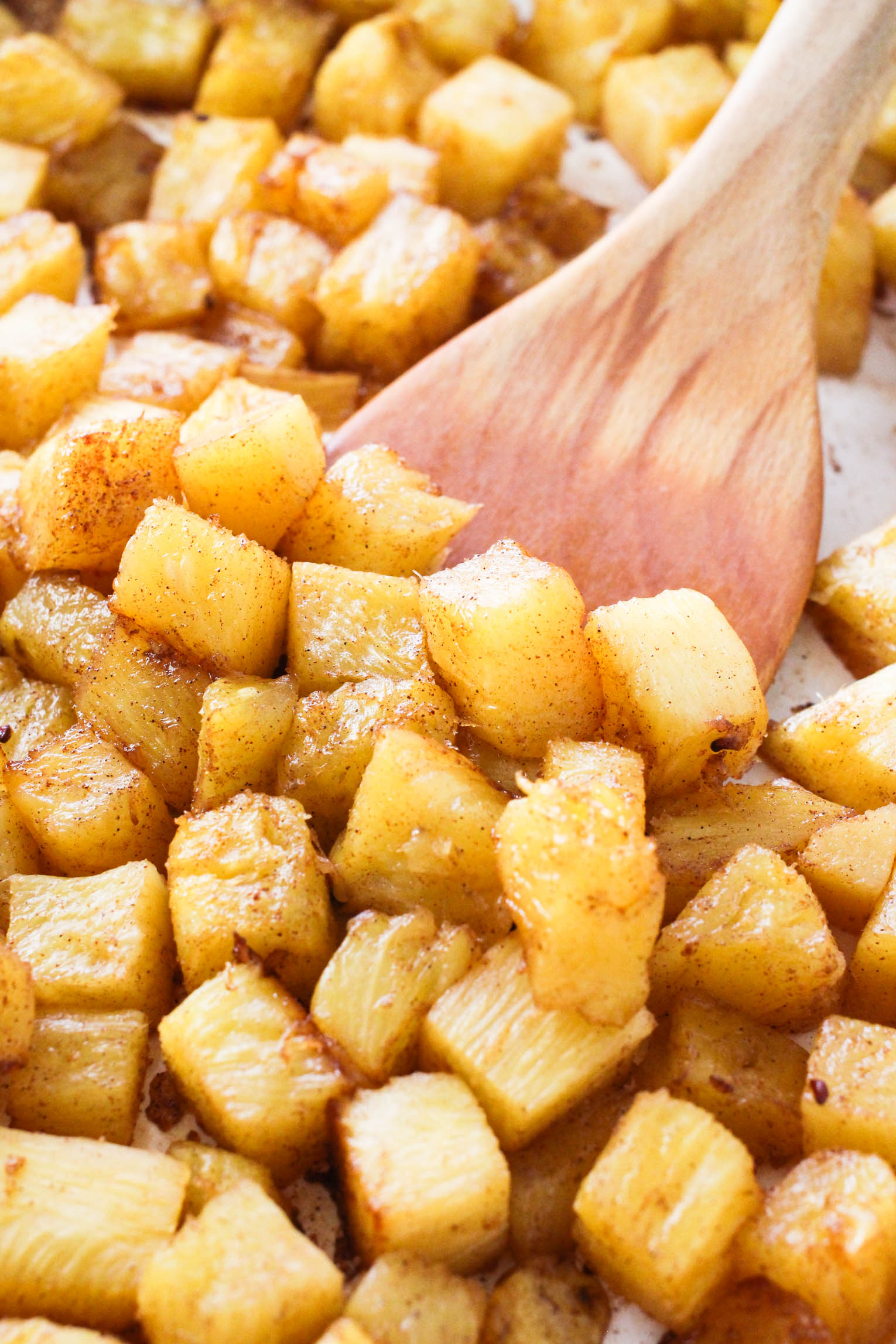 Close up shot of roasted pineapple slices being scooped with a wooden spatula.