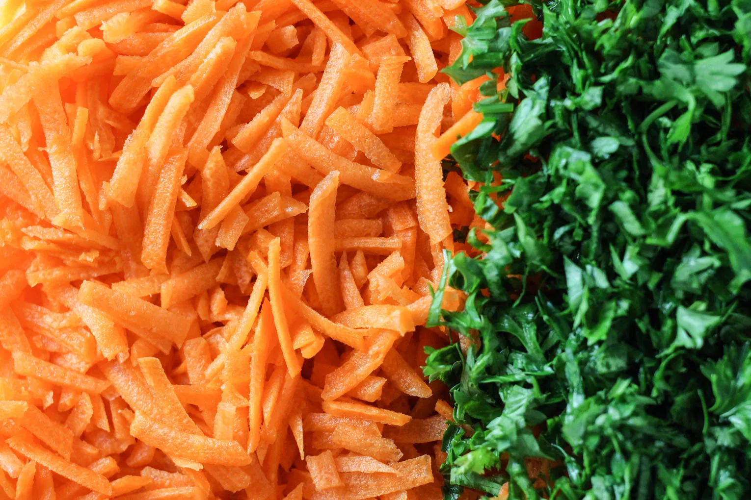 Close up shot of grated carrots on the left and chopped parsley on the right.