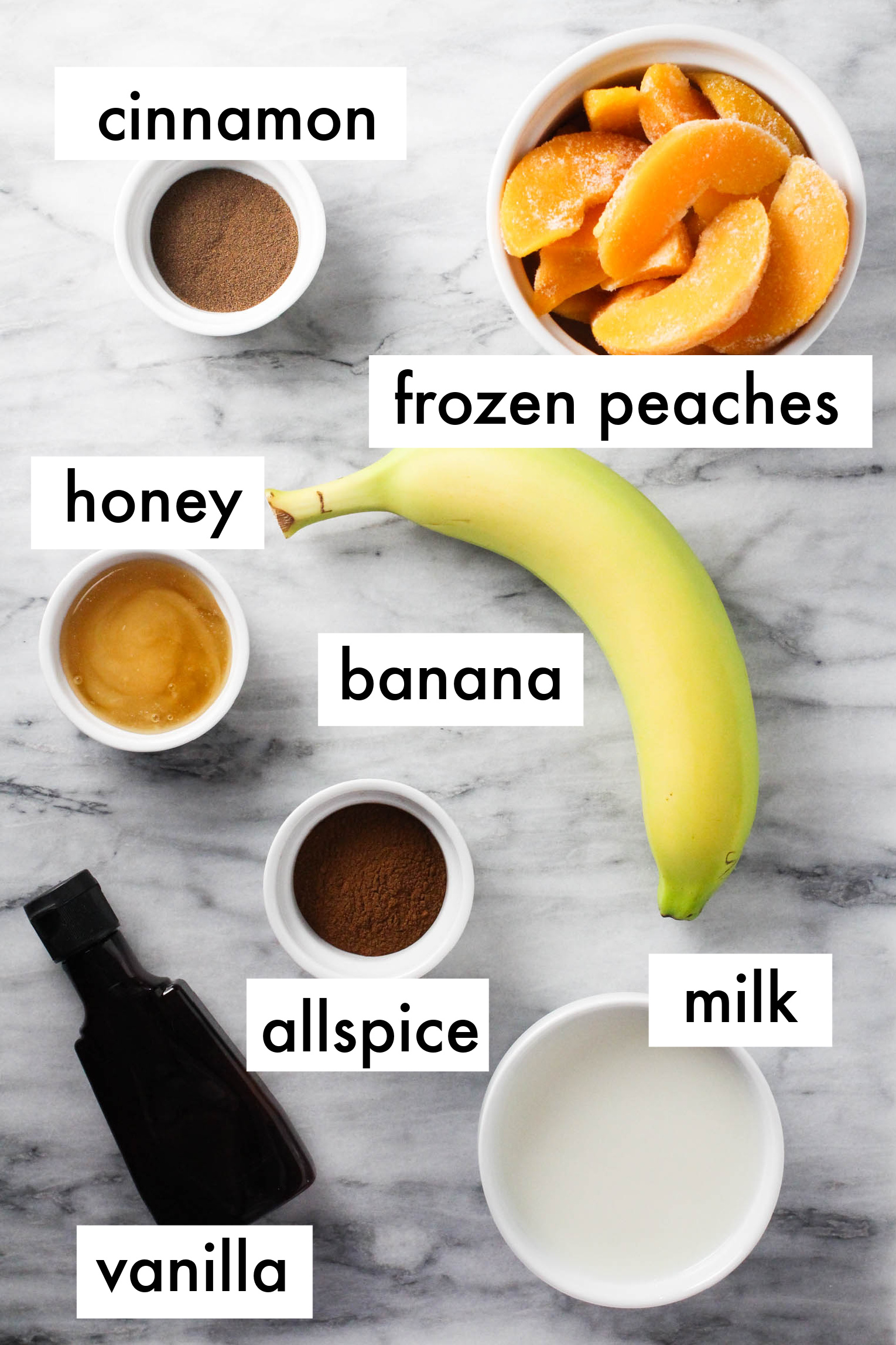 Peach banana smoothie ingredients displayed on marble background. The ingredients are labeled as follows: cinnamon, frozen peaches, honey, banana, allspice, milk, vanilla.