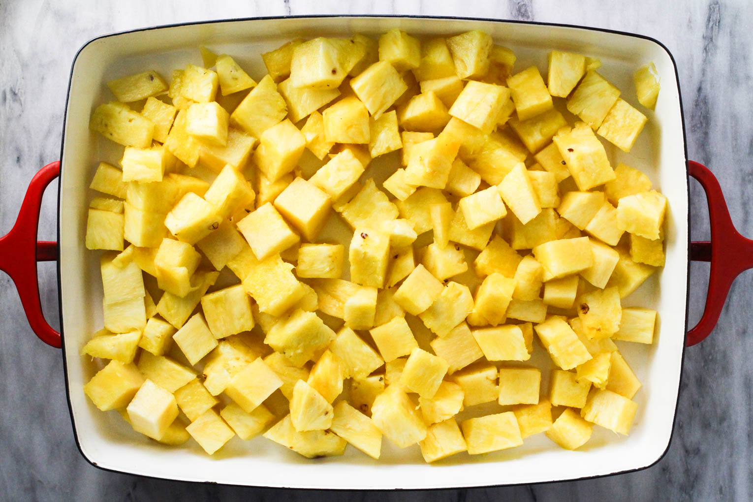 Overhead shot of pineapple slices in a baking dish standing on marble background.