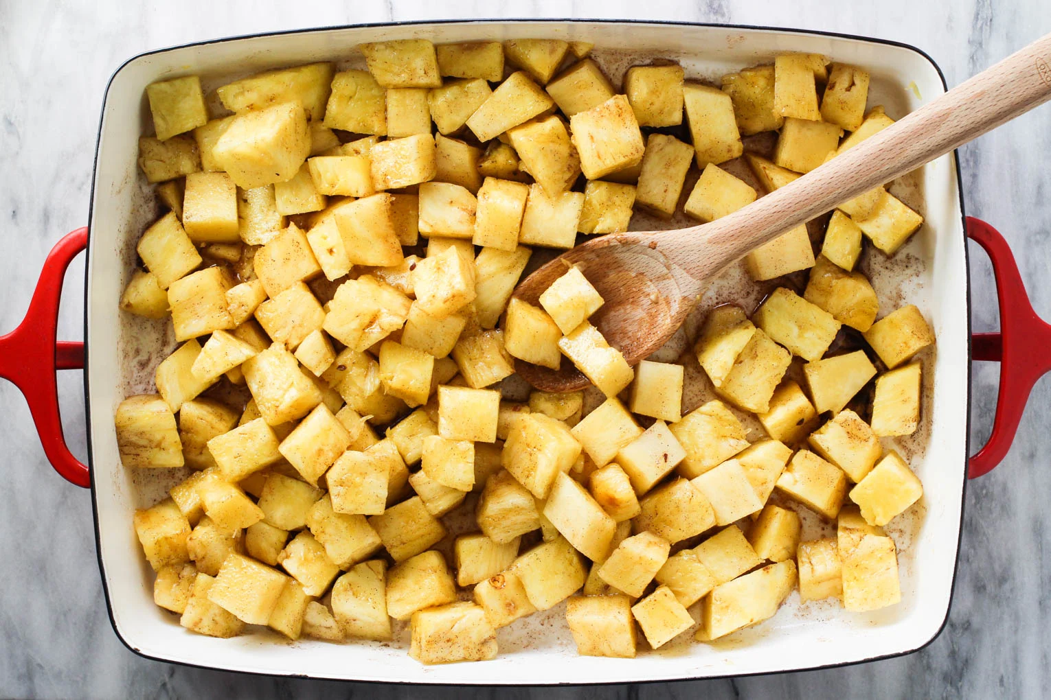 Pineapple slices in a baking dish being mixed with the glaze with a wooden spoon.