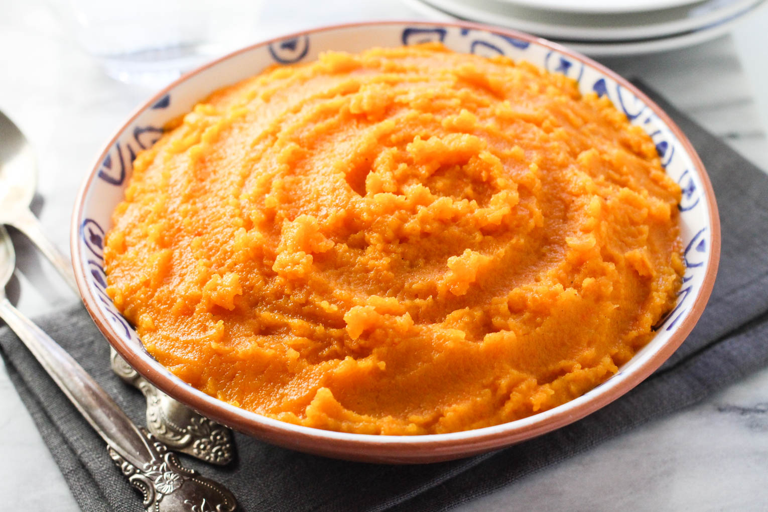 Carrot and swede mash in a bowl standing on a napkin. Two silver spoons the the left.