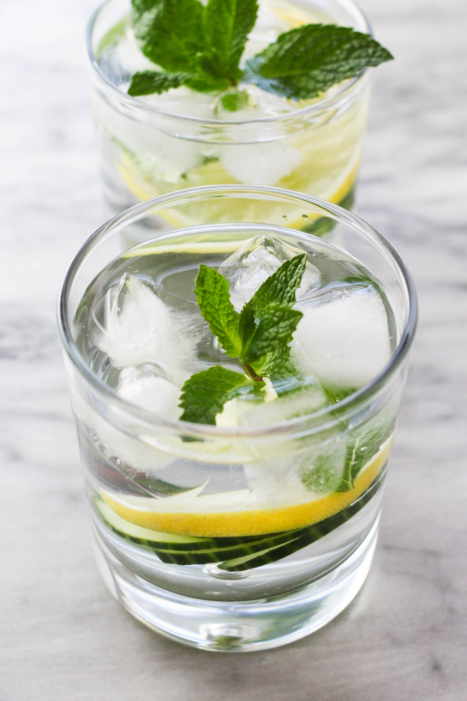 A glass of infused water with ice garnished with mint. Another glass in the background.
