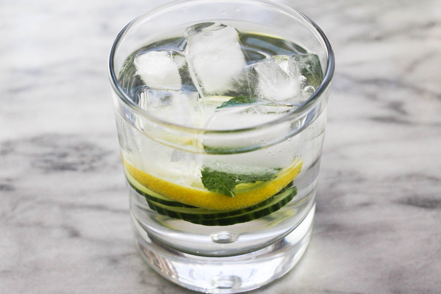 A glass of infused water with ice standing on a marble background.