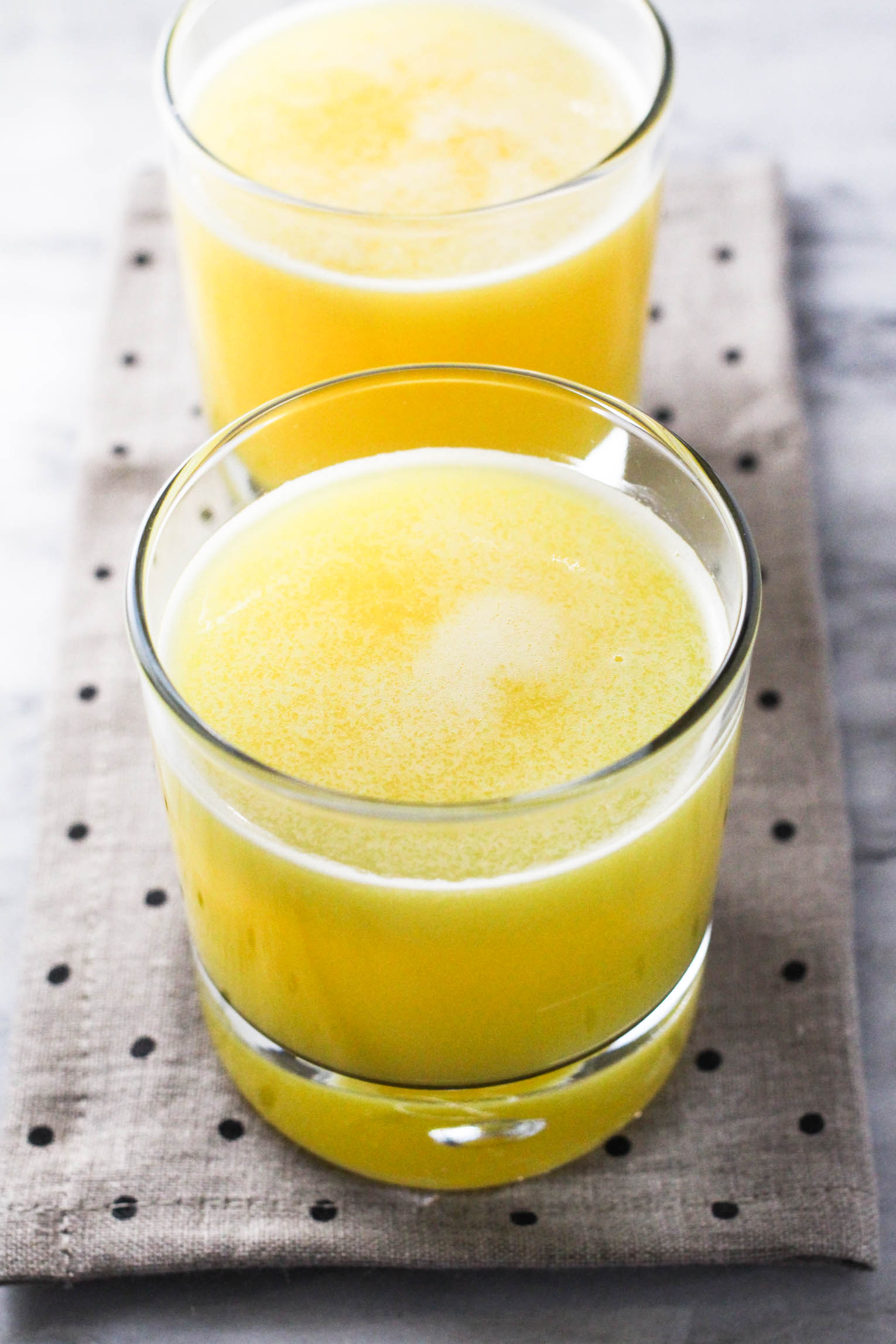 Two glasses of pineapple juice standing on a linen background.