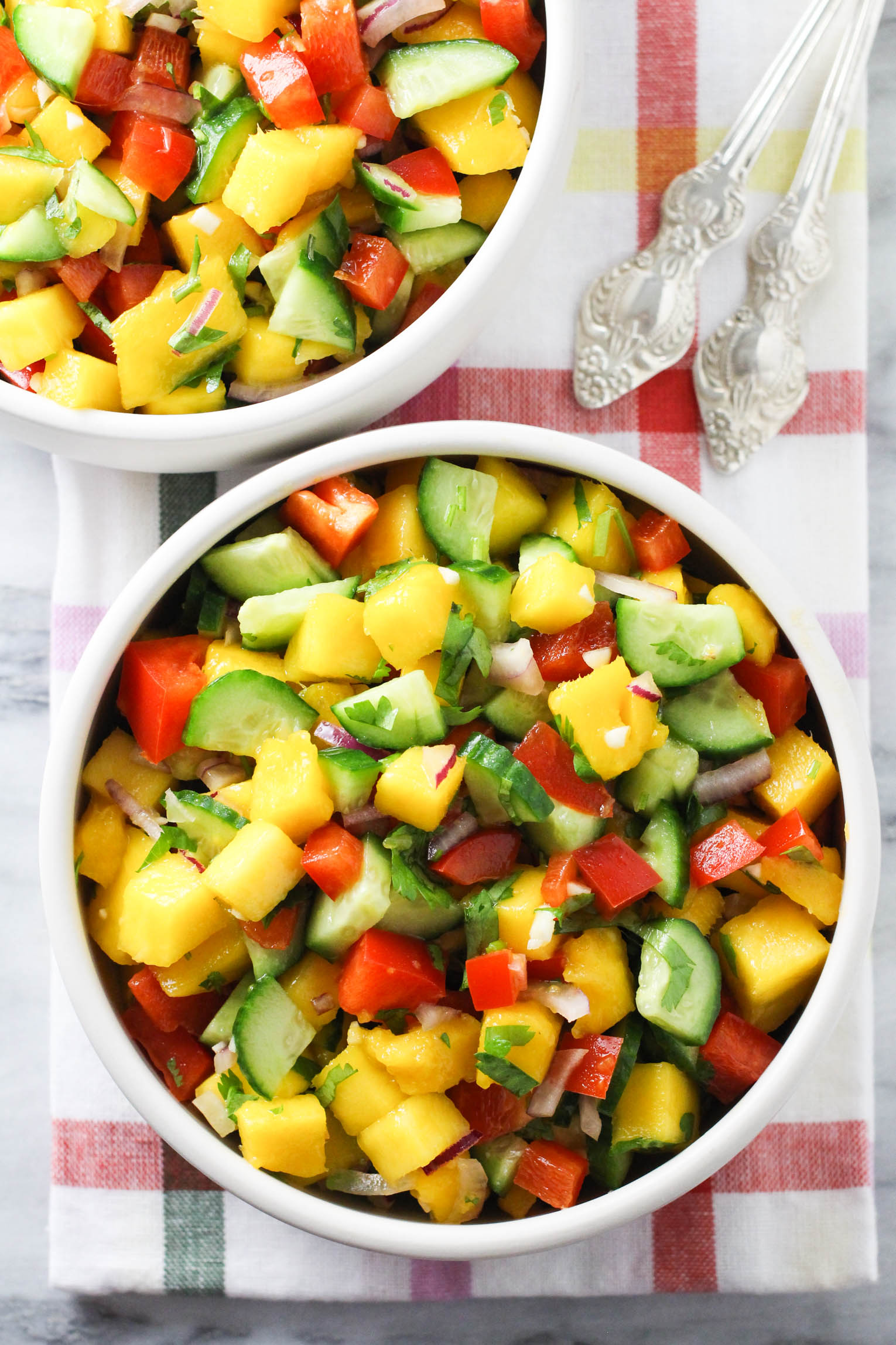 Overhead shot of the mango cucumber salad in a bowl standing on a tea towel.