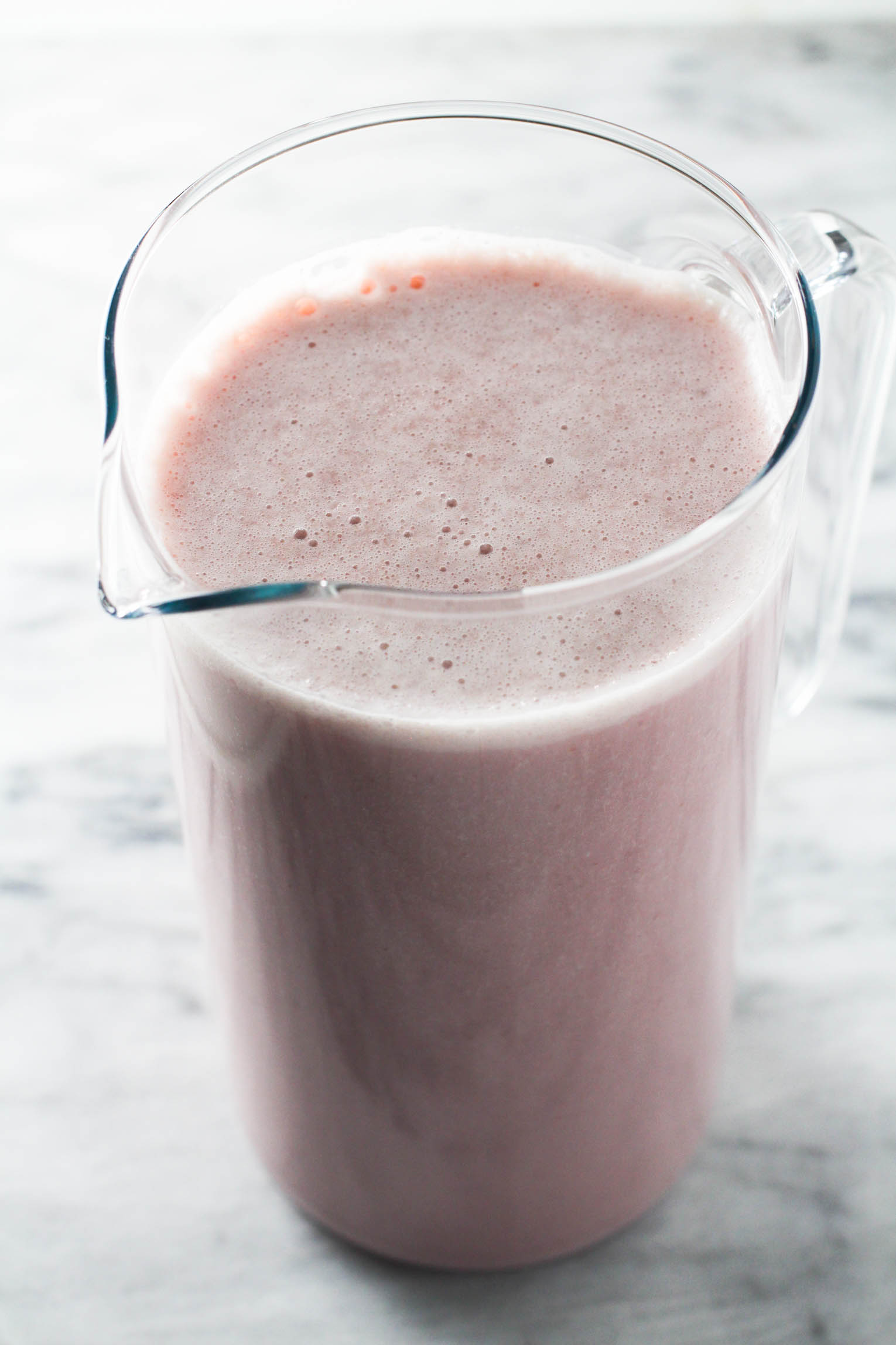 Strawberry milk in a pitcher standing on marble background.