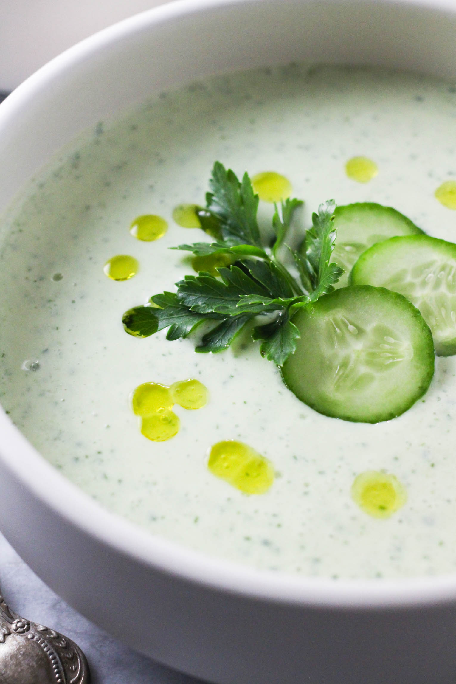Close up shot of the cucumber cottage cheese soup in a bowl. The soup is garnished with cucumber slices, parsley and olive oil.