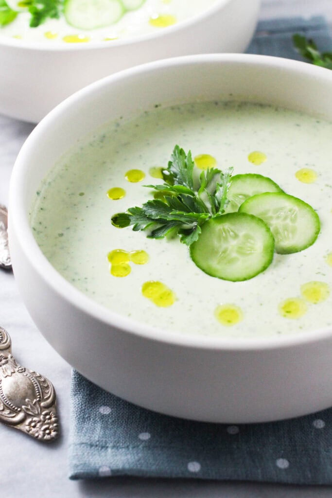 Cucumber Cottage Cheese Soup in a bowl standing on a napkin. The soup is garnished with cucumber slices, parsley and olive oil.