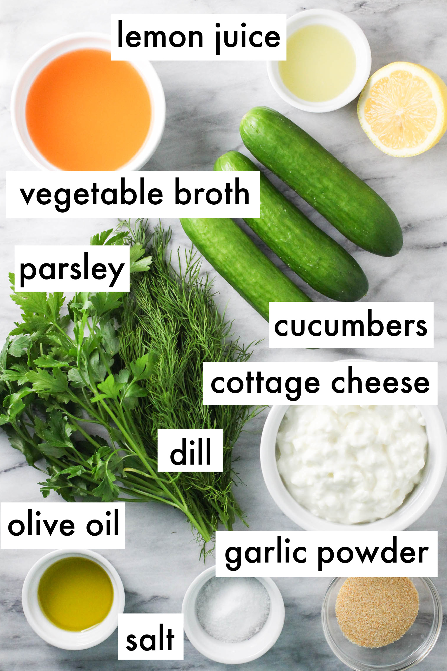 Cottage cheese soup ingredients displayed on marble background. The ingredients are labeled as follows: lemon juice, vegetable broth, parsley, cucumbers, cottage cheese, dill, olive oil, garlic powder, salt.