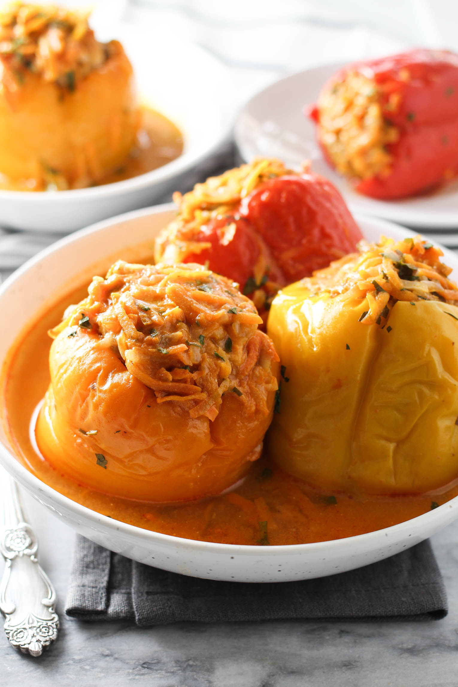 Three stuffed bell peppers in a bowl standing on a napkin. Two more stuffed peppers on plates in the background.