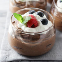 Cottage cheese chocolate mousse in a glass bowl garnished with whipped cream, raspberry, blueberry and mind leaves.