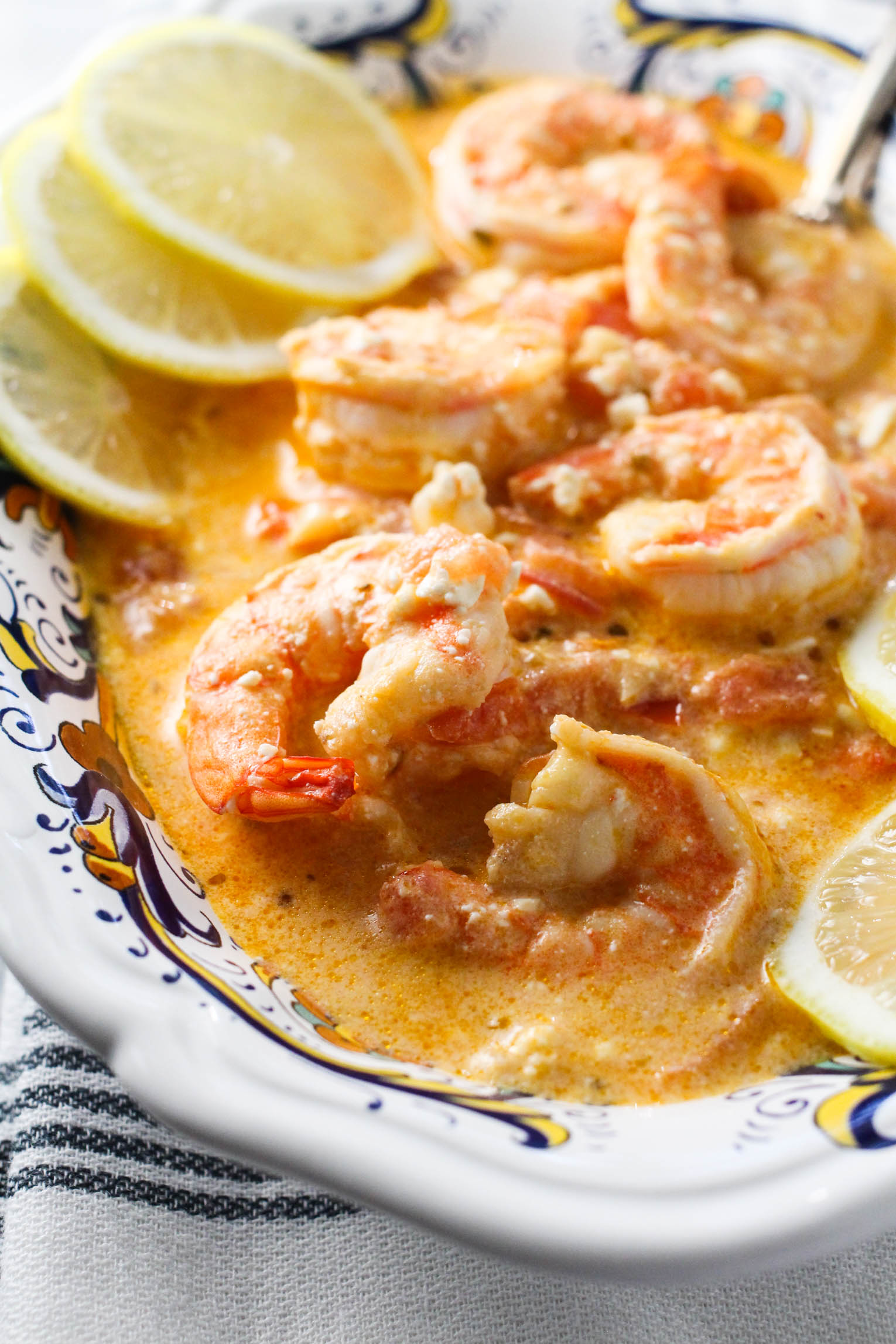Shrimp with feta and tomatoes in a bowl garnished with lemon slices.