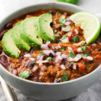 Tuna chili in a bowl garnished with avocado and red onion.